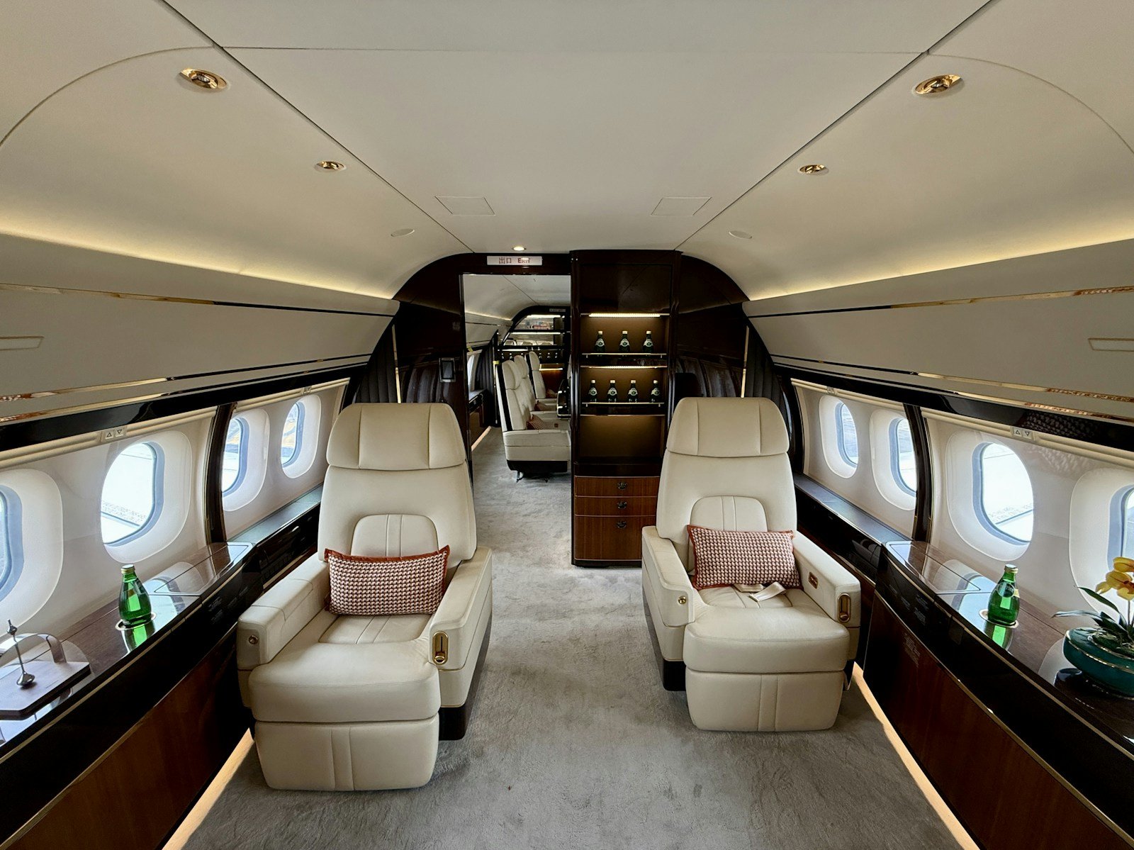 Ivory club chairs, polished wood and a lit bar cabinet line the long cabin of a private jet.