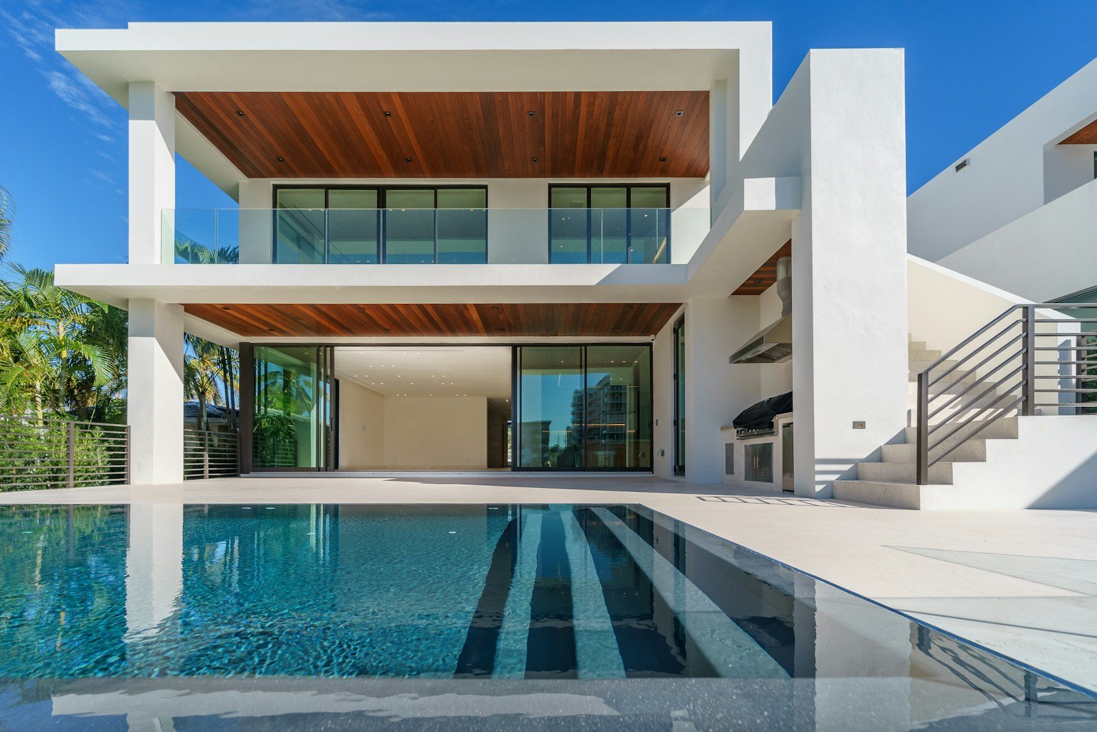 A contemporary white villa with a teak-lined terrace opens onto a long infinity-edge pool under a clear blue sky.