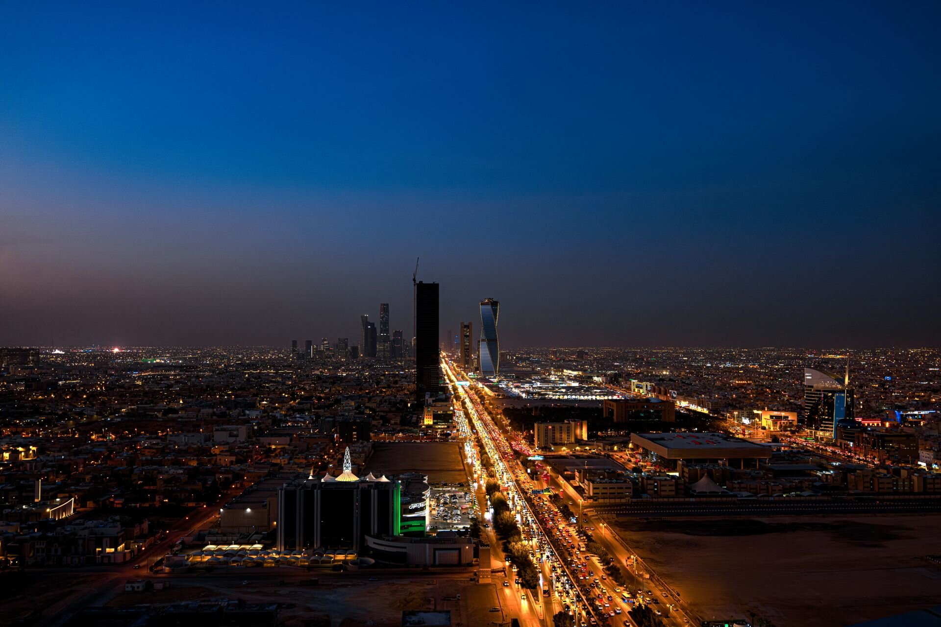 Riyadh at dusk from above, King Fahd Road running toward the new towers of the capital
