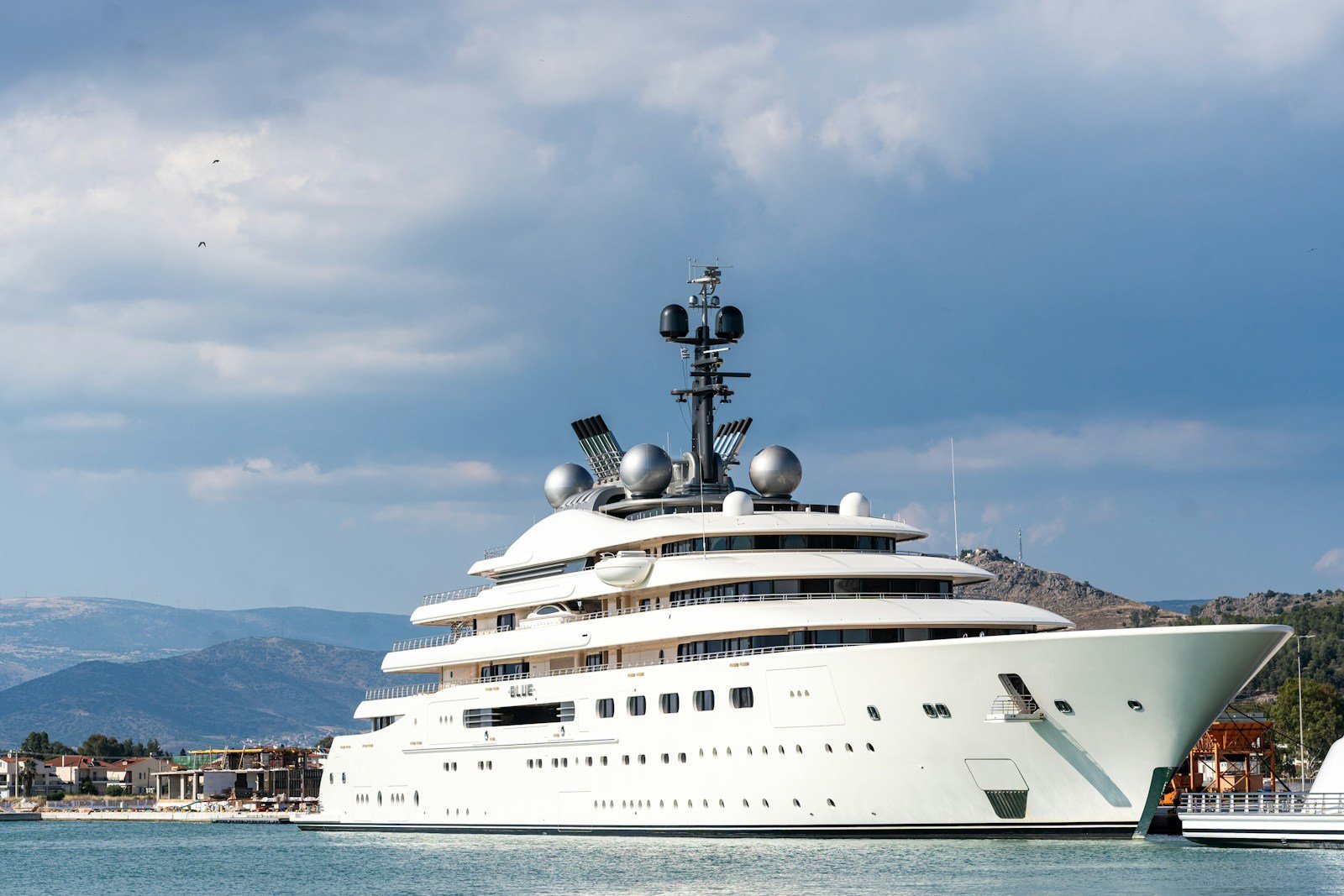 A gleaming white superyacht moored in a quiet bay beneath hills and an open sky.