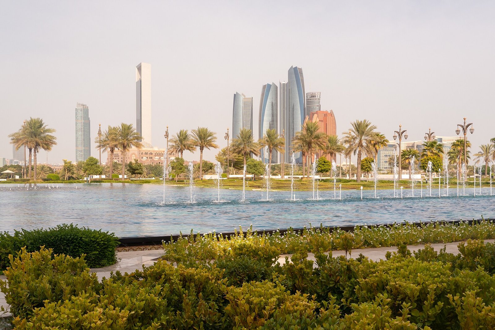 Fountains play across a long pool in the gardens of Qasr Al Watan, with the towers of Abu Dhabi rising beyond the palms.