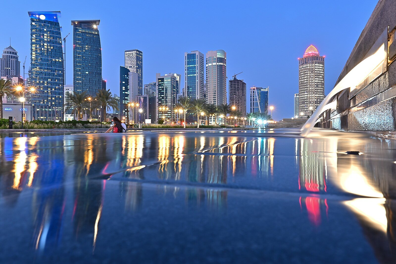 The glass hotel and office towers of Doha's West Bay mirrored in a still water feature at blue hour