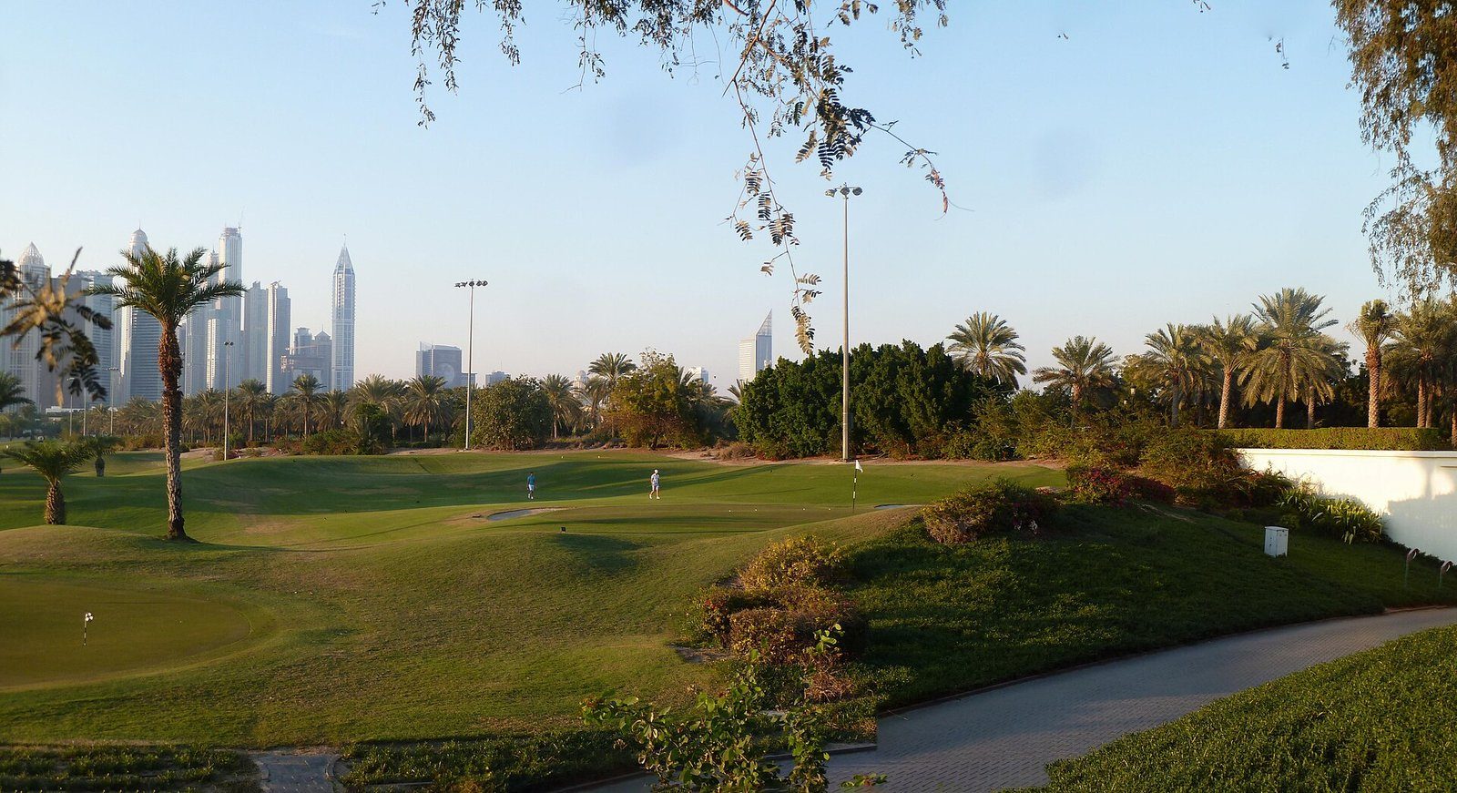 Calles de golf bordeadas de palmeras en Emirates Hills, Dubái, con las torres de Dubai Marina al fondo.