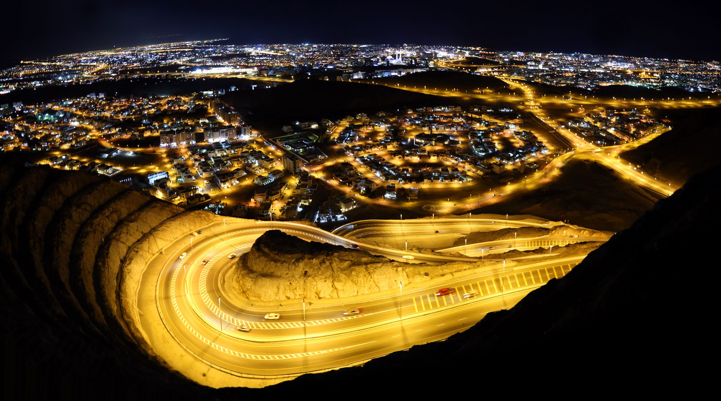 Las luces de la ciudad se extienden por la llanura al pie de las montañas de Omán, de noche