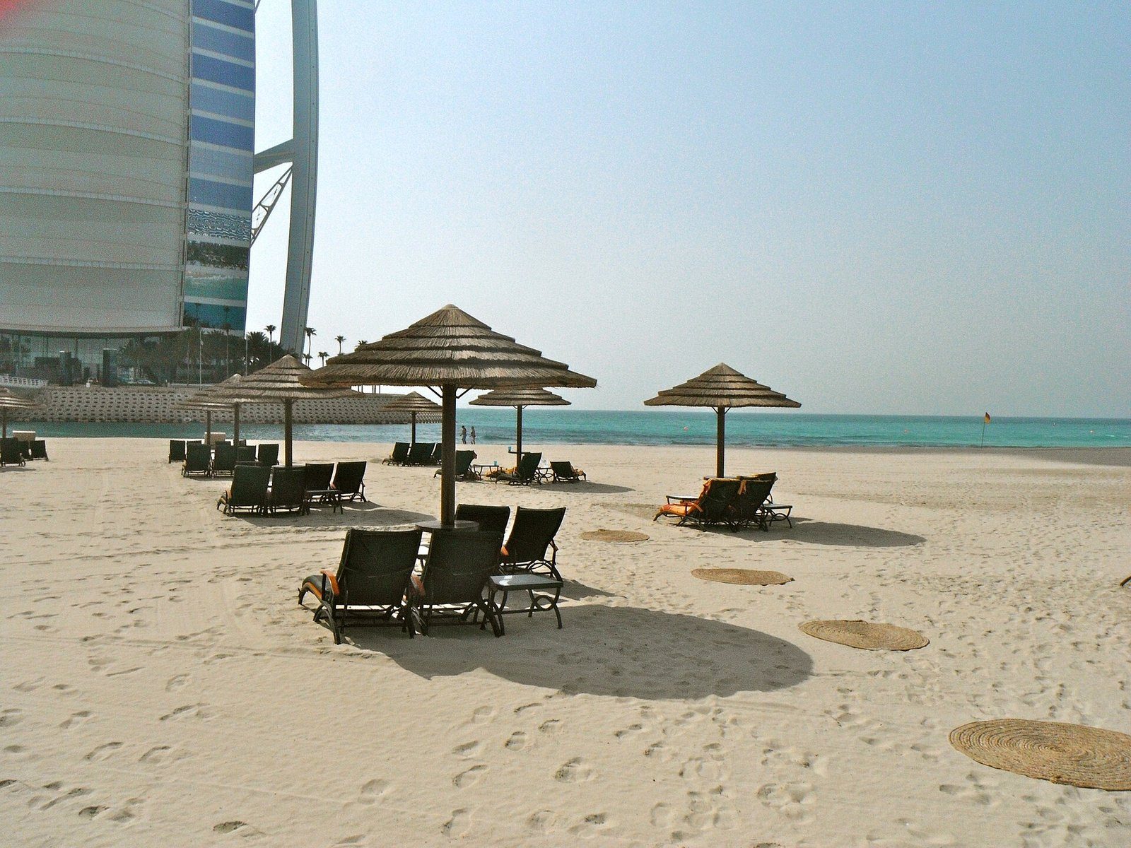 Sombrillas de palma y tumbonas sobre la arena de Jumeirah Beach junto al Burj Al Arab, Dubái.