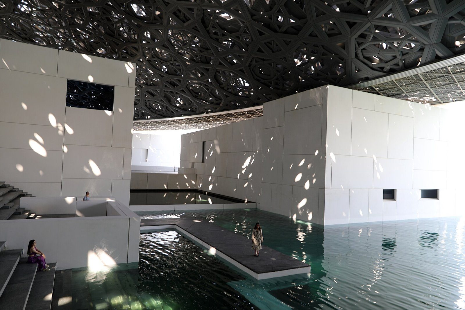 La luz moteada atraviesa la cúpula reticulada del Louvre Abu Dhabi sobre sus galerías blancas y sus estanques en la isla de Saadiyat.