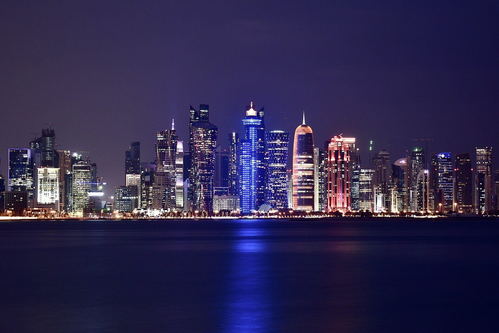 Las torres de West Bay en Doha iluminadas de noche y reflejadas en la bahía.