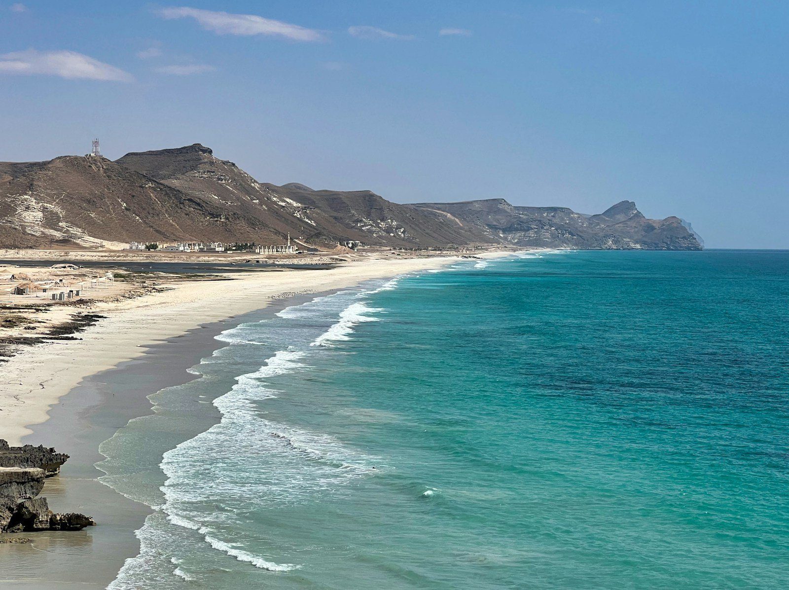 Una larga playa de arena blanca y oleaje turquesa al pie de las montañas cerca de Salalah, Omán