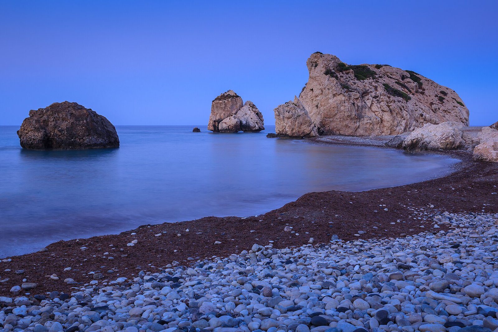 Petra tou Romiou, la Roca de Afrodita, emergiendo de un mar en calma en la hora azul previa al amanecer en la costa de Pafos, Chipre.