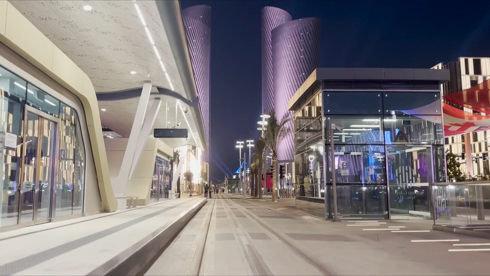 Las Lusail Plaza Towers resplandeciendo sobre las tiendas y el paseo de Lusail Boulevard de noche.