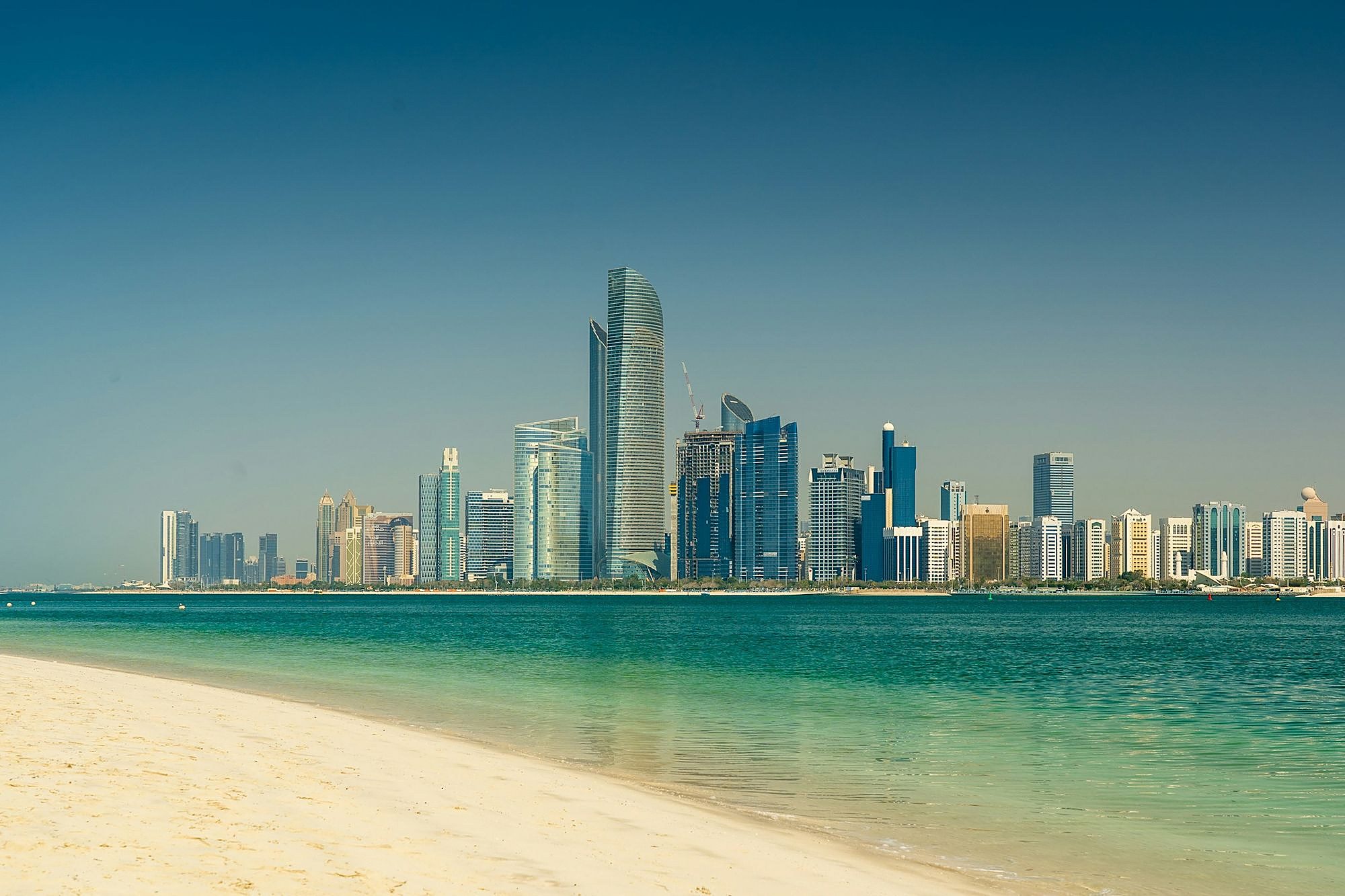 Las torres de Abu Dabi alzándose al otro lado de aguas turquesas desde una playa de arena blanca