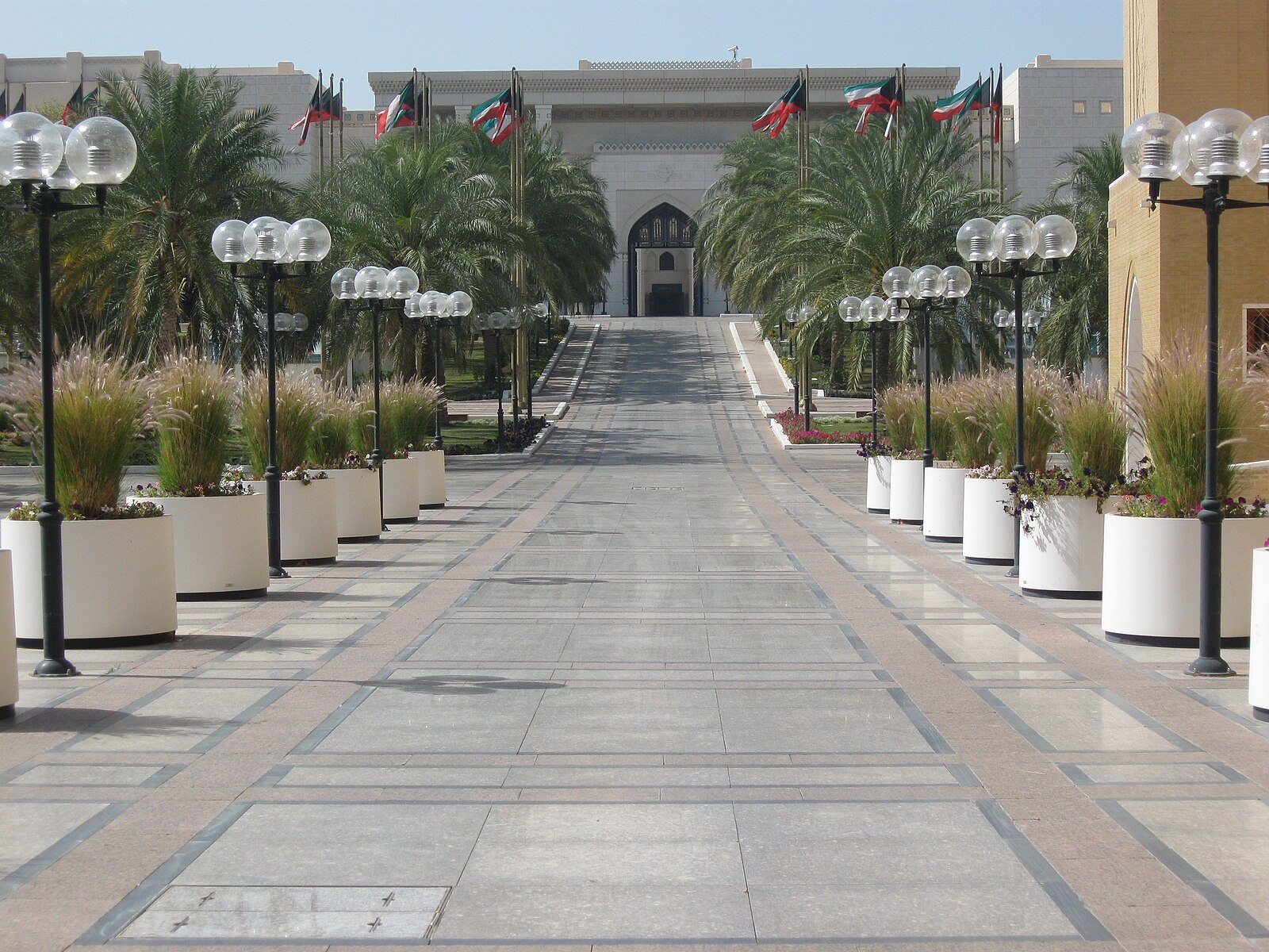Un acceso bordeado de palmeras, con faroles y banderas kuwaitíes, que conduce al Palacio Seif en la ciudad de Kuwait.