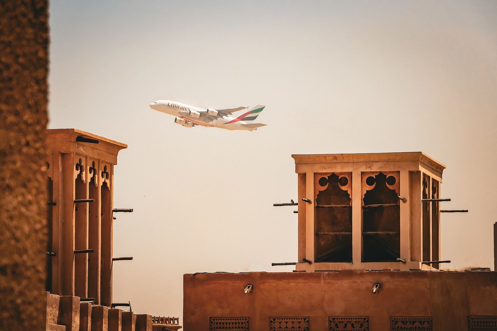 Un A380 de Emirates sobrevuela las torres de viento del barrio histórico de Al Fahidi, en Dubái, bajo la cálida luz del atardecer.