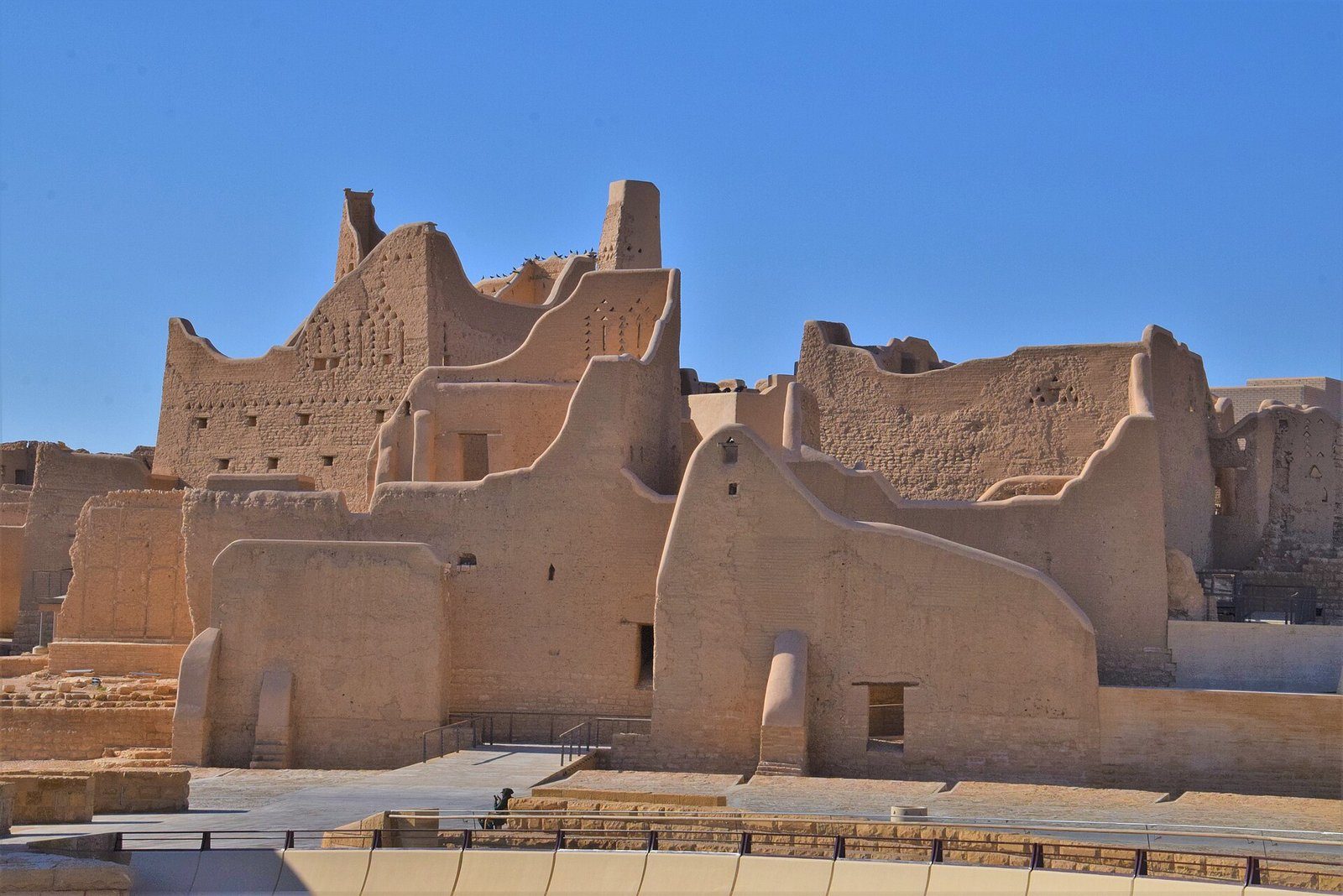 Los muros y torres de adobe del Palacio de Salwa en el distrito de At-Turaif de Diriyah bajo un cielo azul despejado.