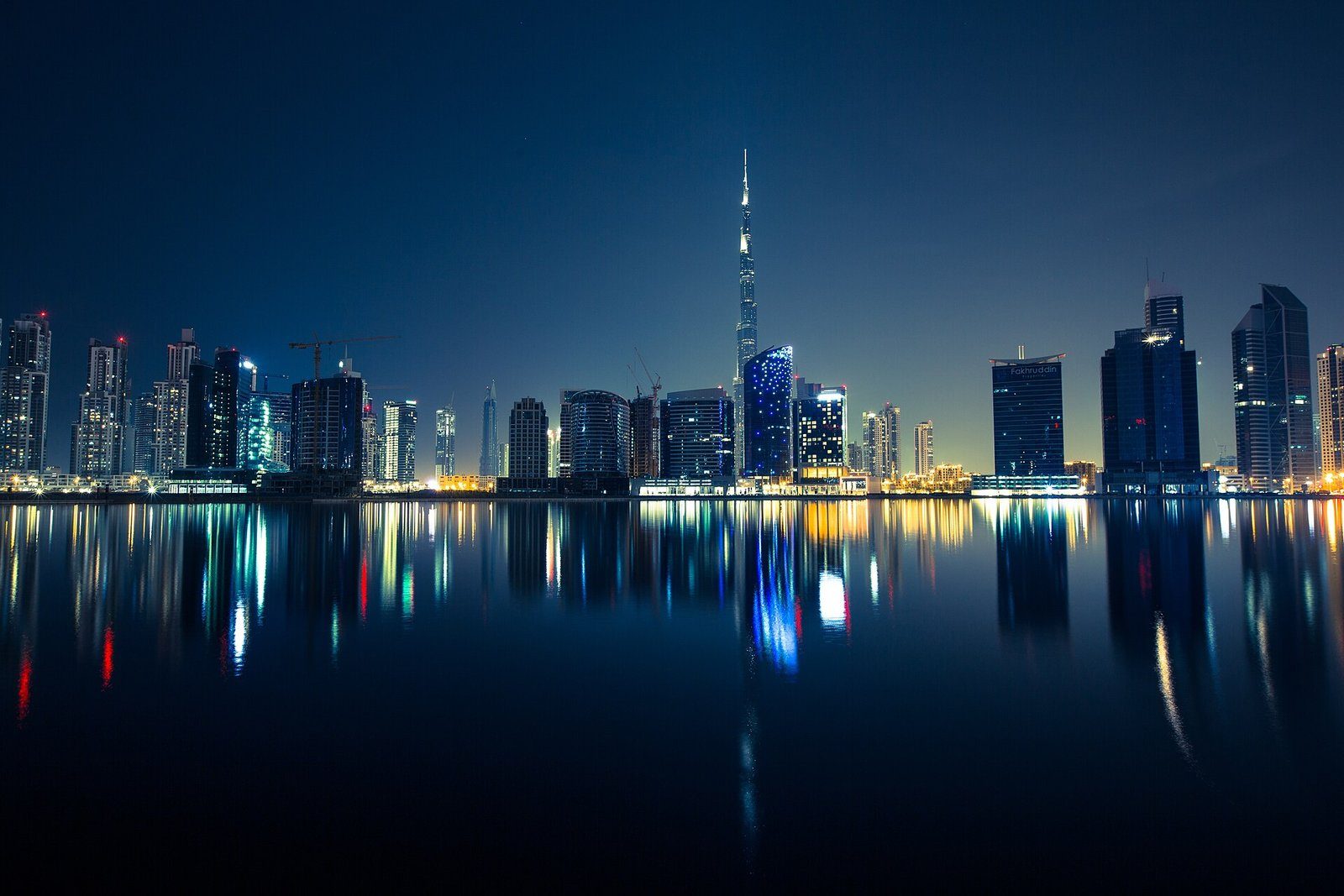 El perfil urbano de Dubái y el Burj Khalifa reflejados en el agua quieta de noche.