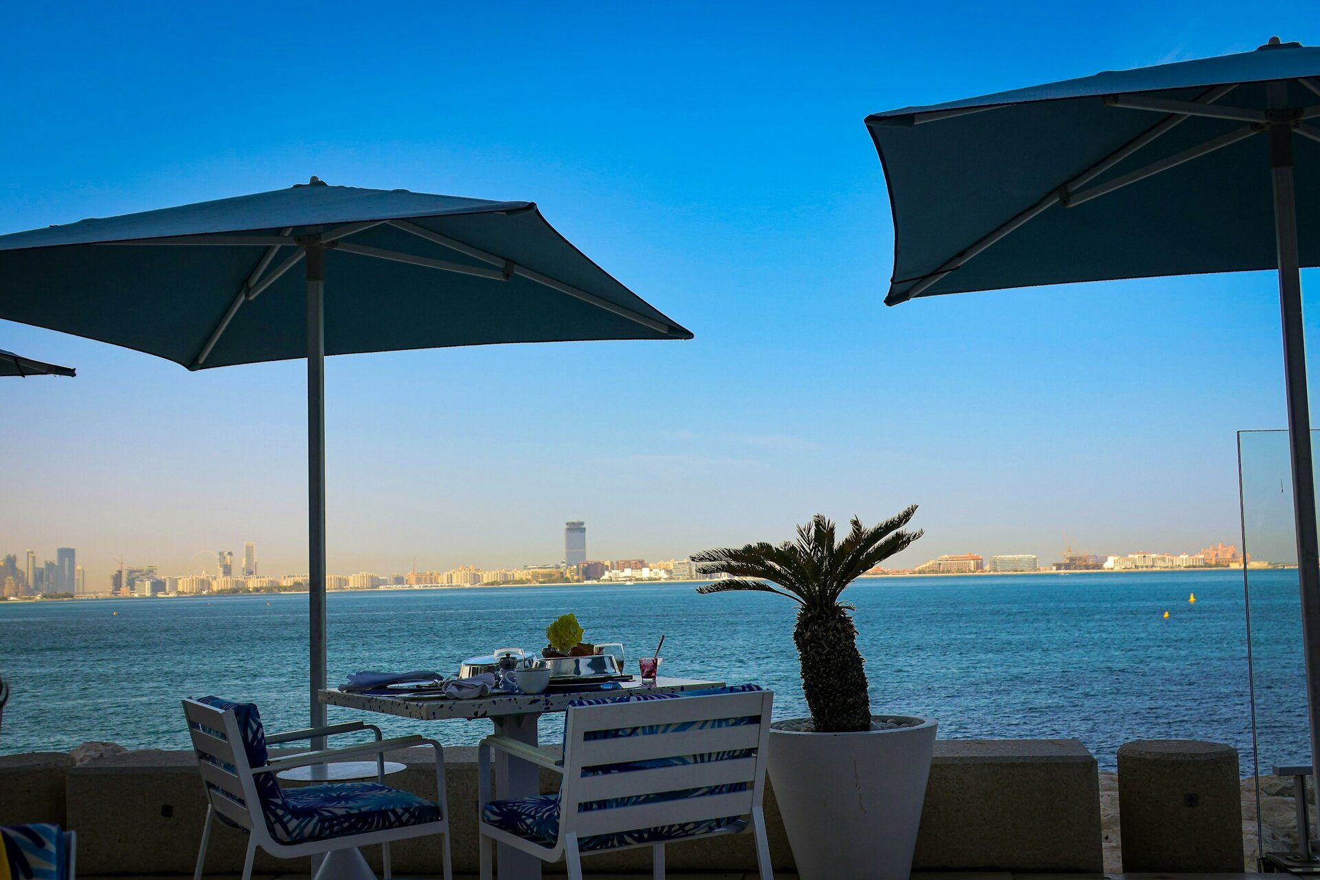 Una mesa bajo sombrillas en una terraza frente al mar, con vistas a Palm Jumeirah, Dubái