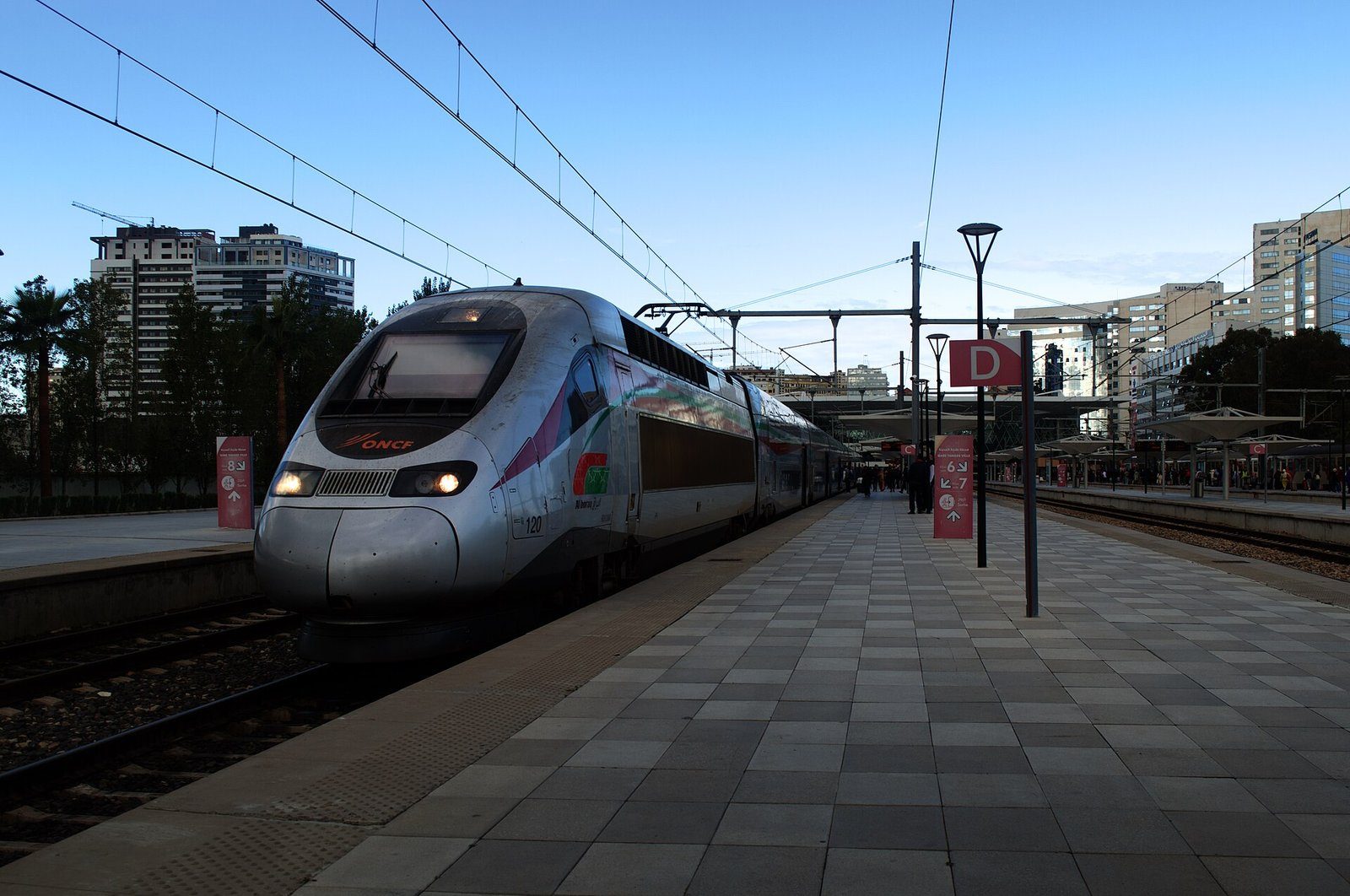 Un tren de alta velocidad Al Boraq plateado esperando en el andén de la estación de Tanger-Ville bajo un cielo azul.