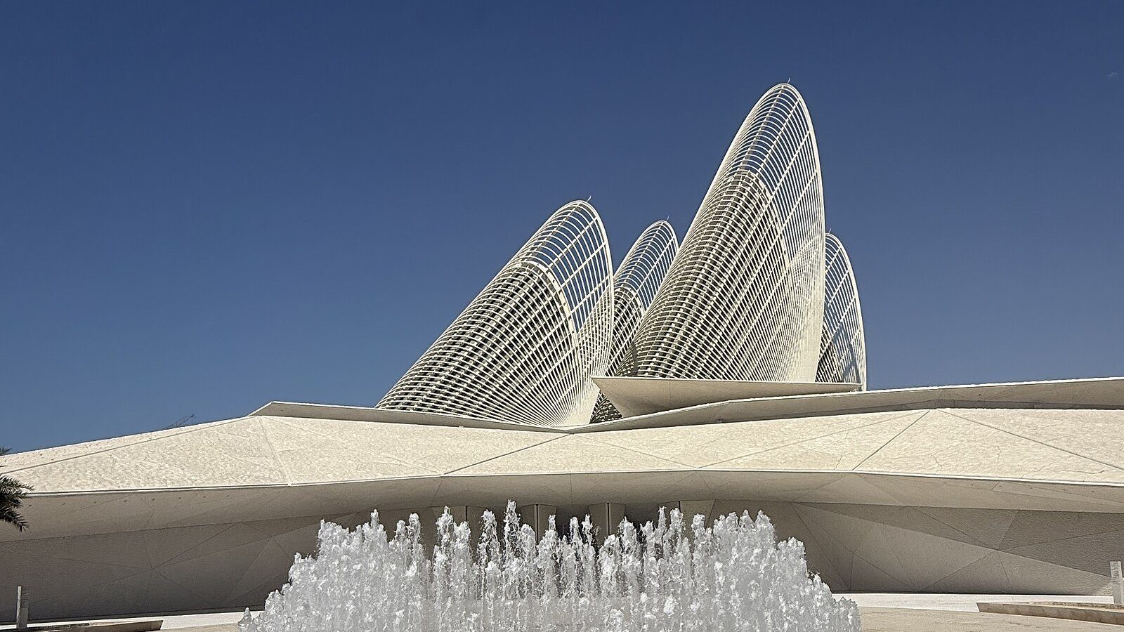 Las torres en forma de pluma de halcón del Zayed National Museum alzándose sobre una fuente en la isla de Saadiyat bajo un cielo azul intenso