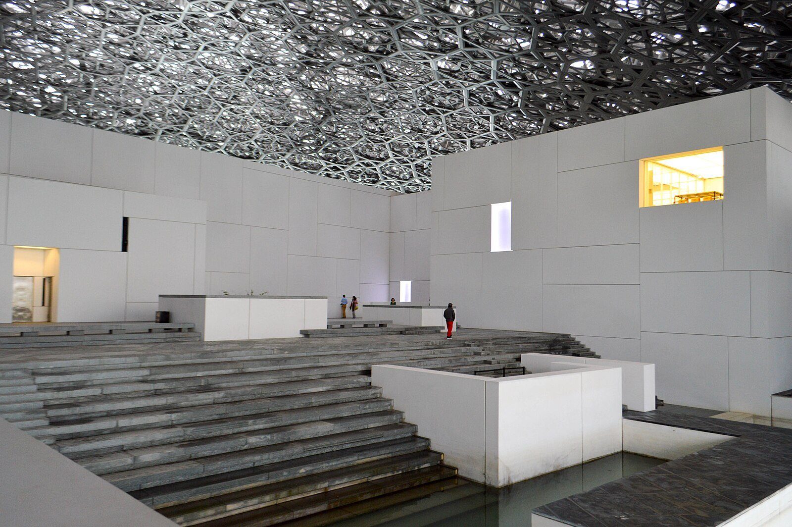 Terrazas escalonadas de piedra y pabellones blancos de galerías bajo la cúpula calada como un encaje del Louvre Abu Dhabi