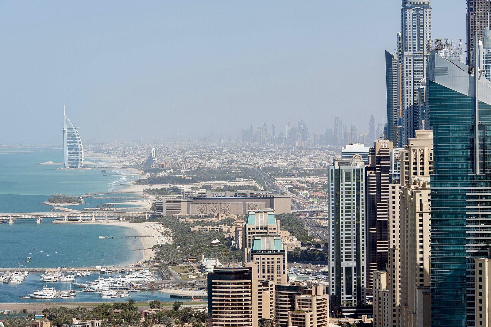 La costa de Dubái curvándose hacia la vela del Burj Al Arab, con las torres de la marina y las playas a sus pies.
