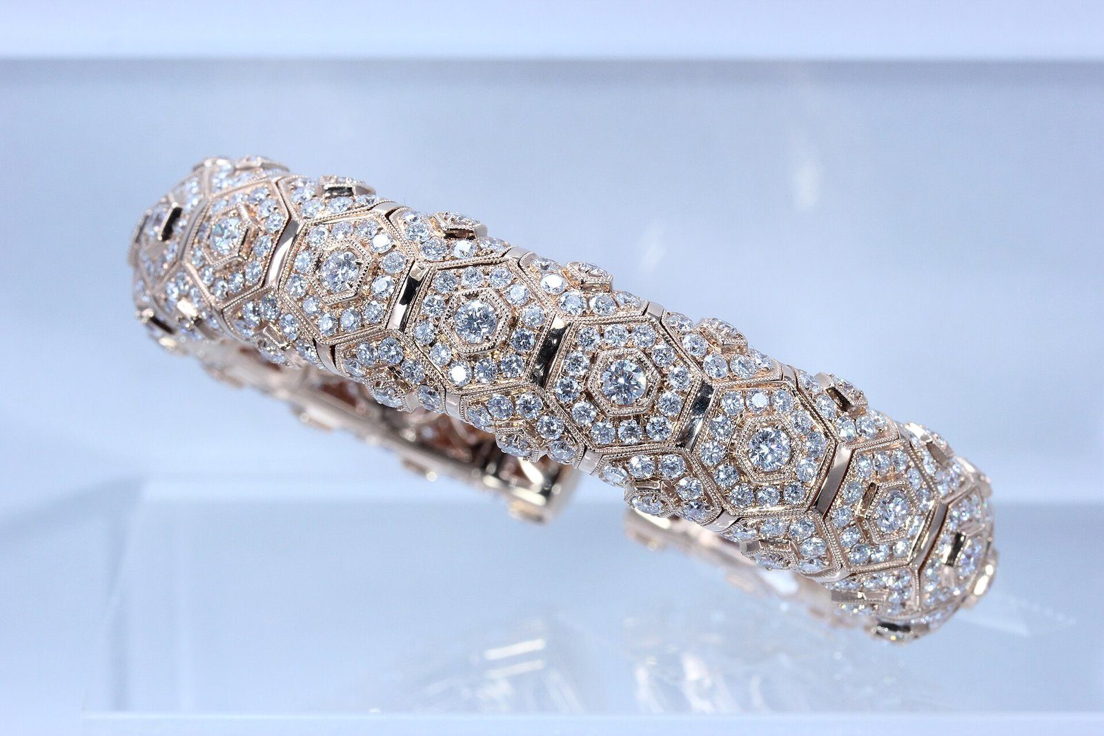 Una pulsera de oro rosa engastada con grupos hexagonales de diamantes, sobre un fondo azul claro.