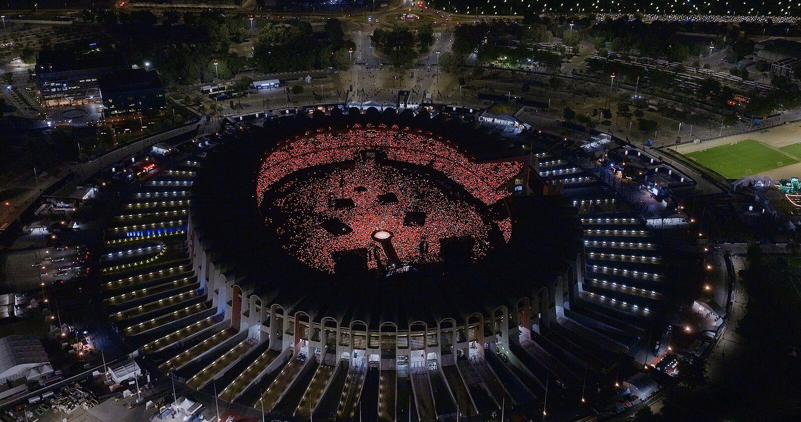El Zayed Sports City Stadium de Abu Dabi visto desde arriba de noche, con su graderío iluminado en rojo durante un concierto.