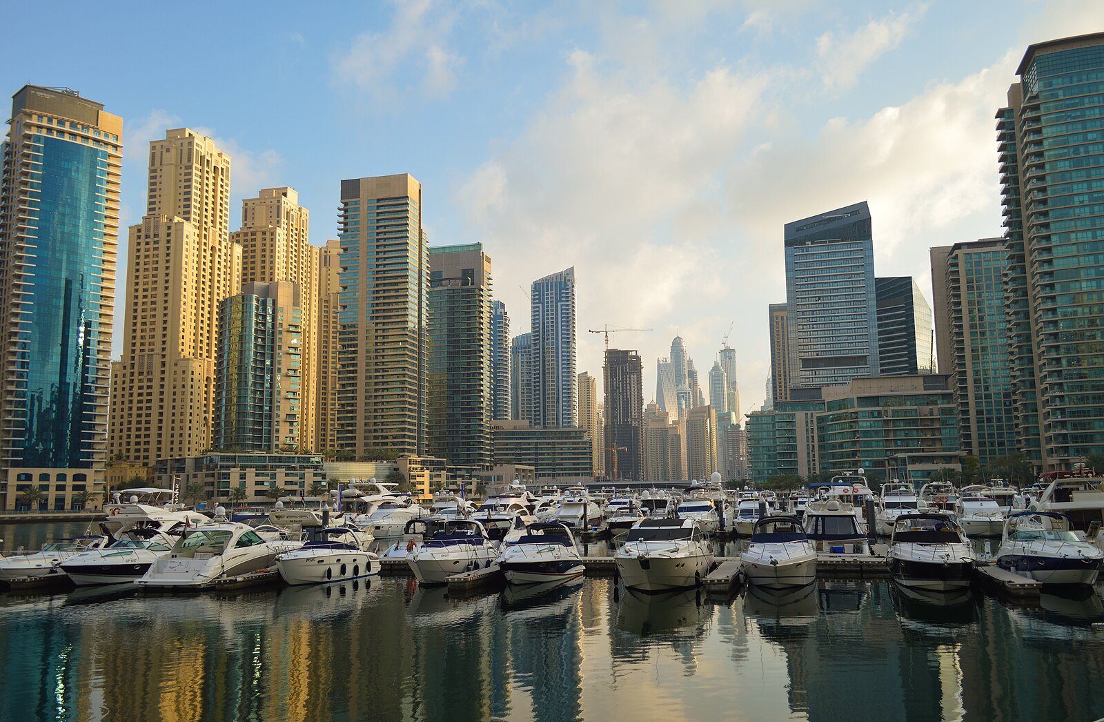 Yates amarrados en Dubai Marina bajo sus torres residenciales, reflejados en el agua quieta.