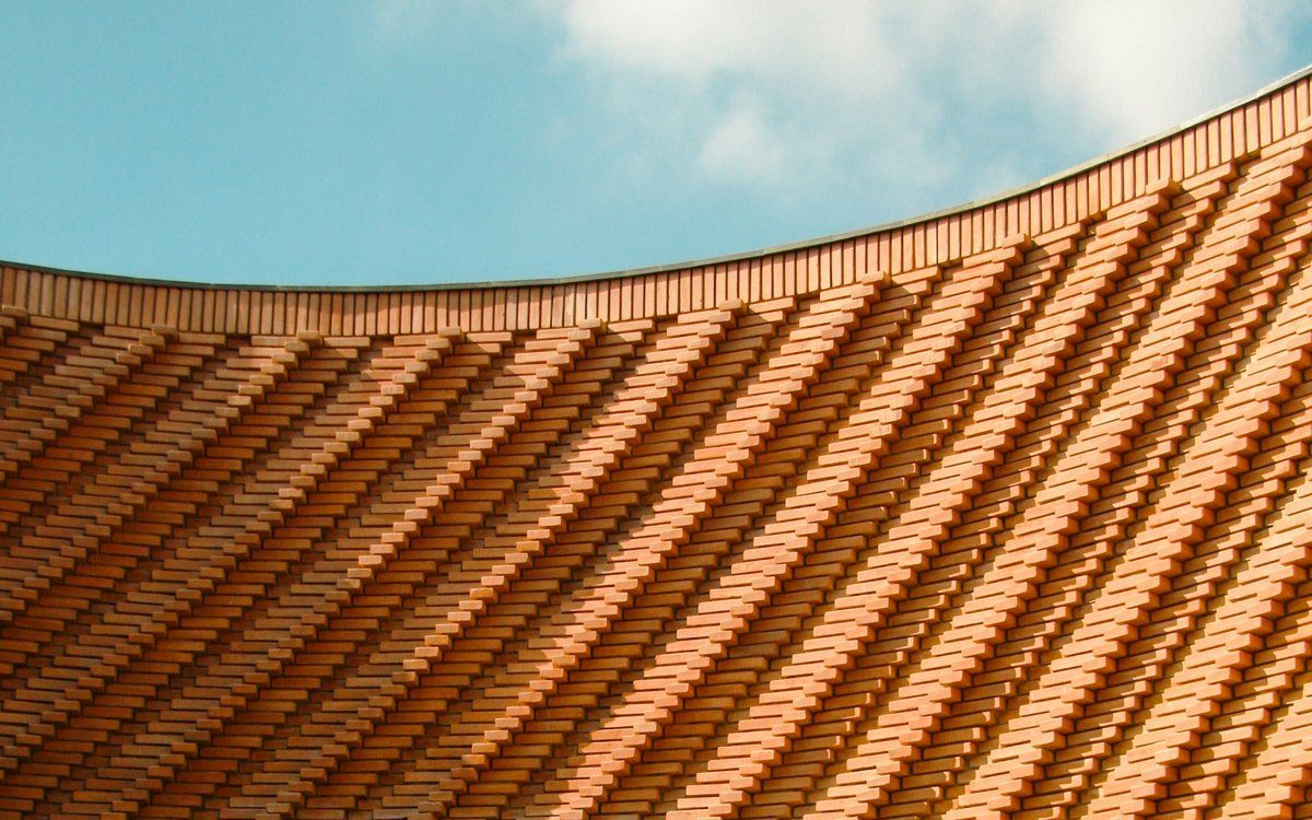 La celosía curva de ladrillo terracota del Musée Yves Saint Laurent Marrakech bajo un suave cielo azul.