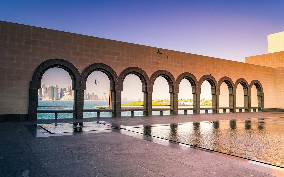 La logia arqueada del Museo de Arte Islámico enmarca el horizonte de Doha al otro lado de la bahía al anochecer.