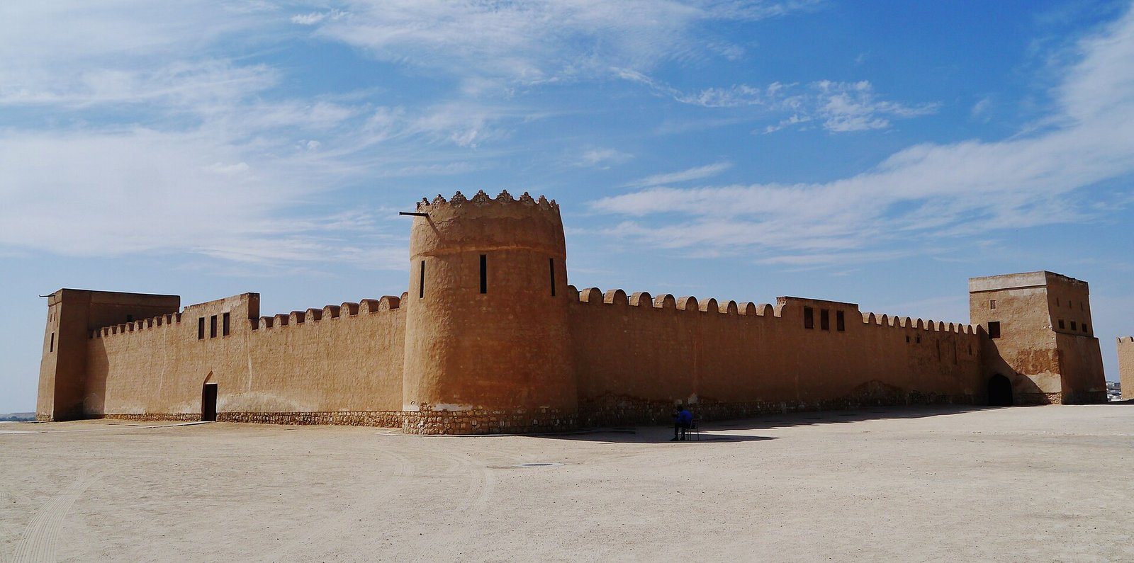 Las murallas color arena y la torre redonda del Fuerte de Riffa, el Fuerte Sheikh Salman bin Ahmed Al Fateh, en Baréin bajo un cielo azul.