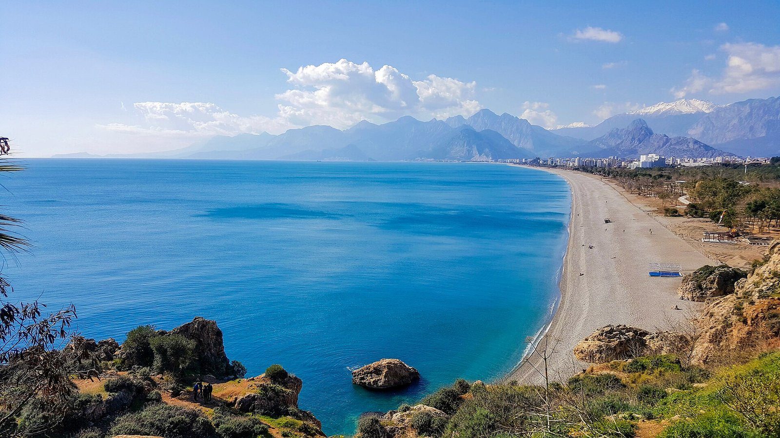 La larga curva de la playa de Konyaalti y sus aguas turquesas bajo los montes Bey, vistas desde los acantilados de Antalya.