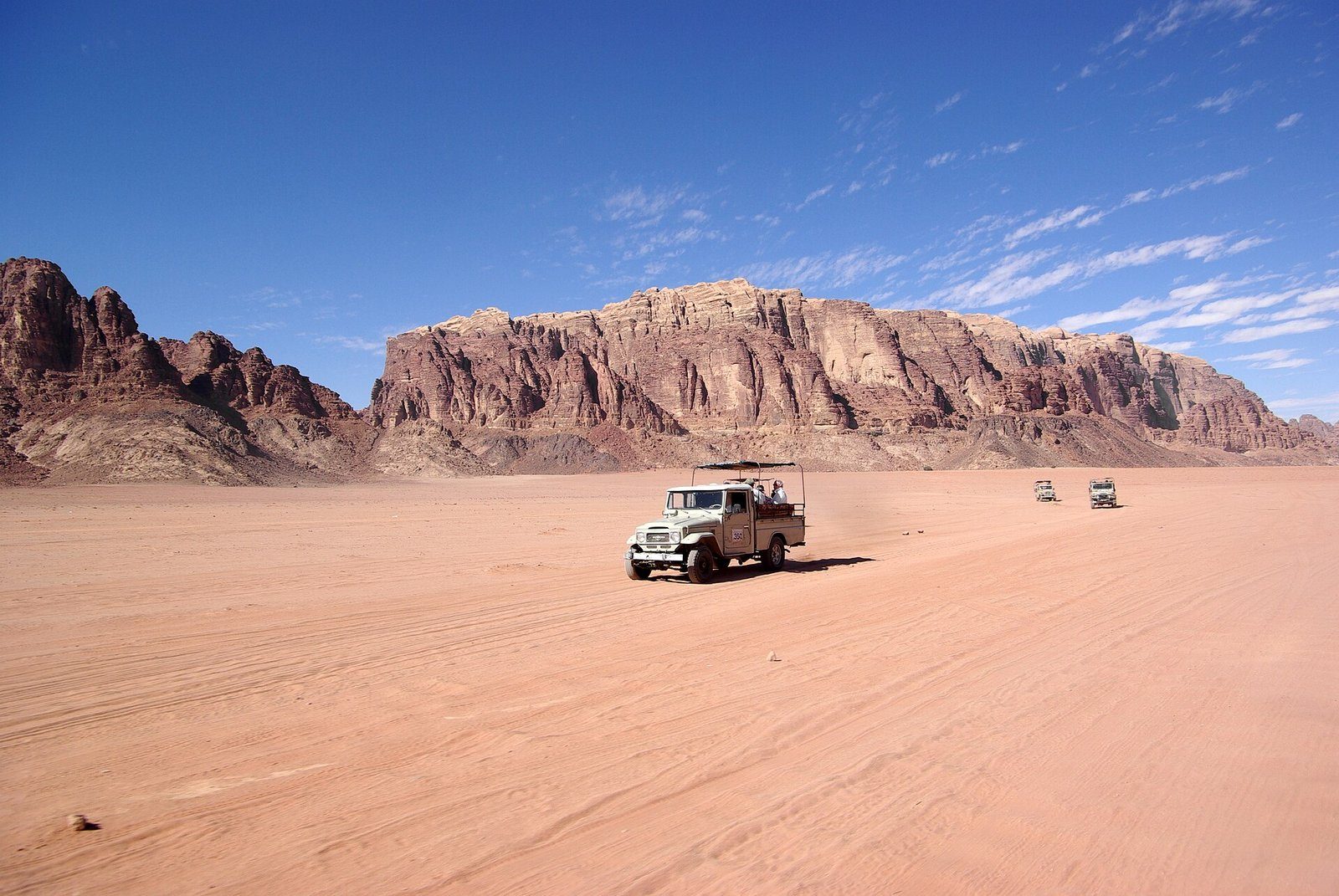Un 4x4 cruzando las arenas rojas de Wadi Rum bajo altísimos acantilados de arenisca.