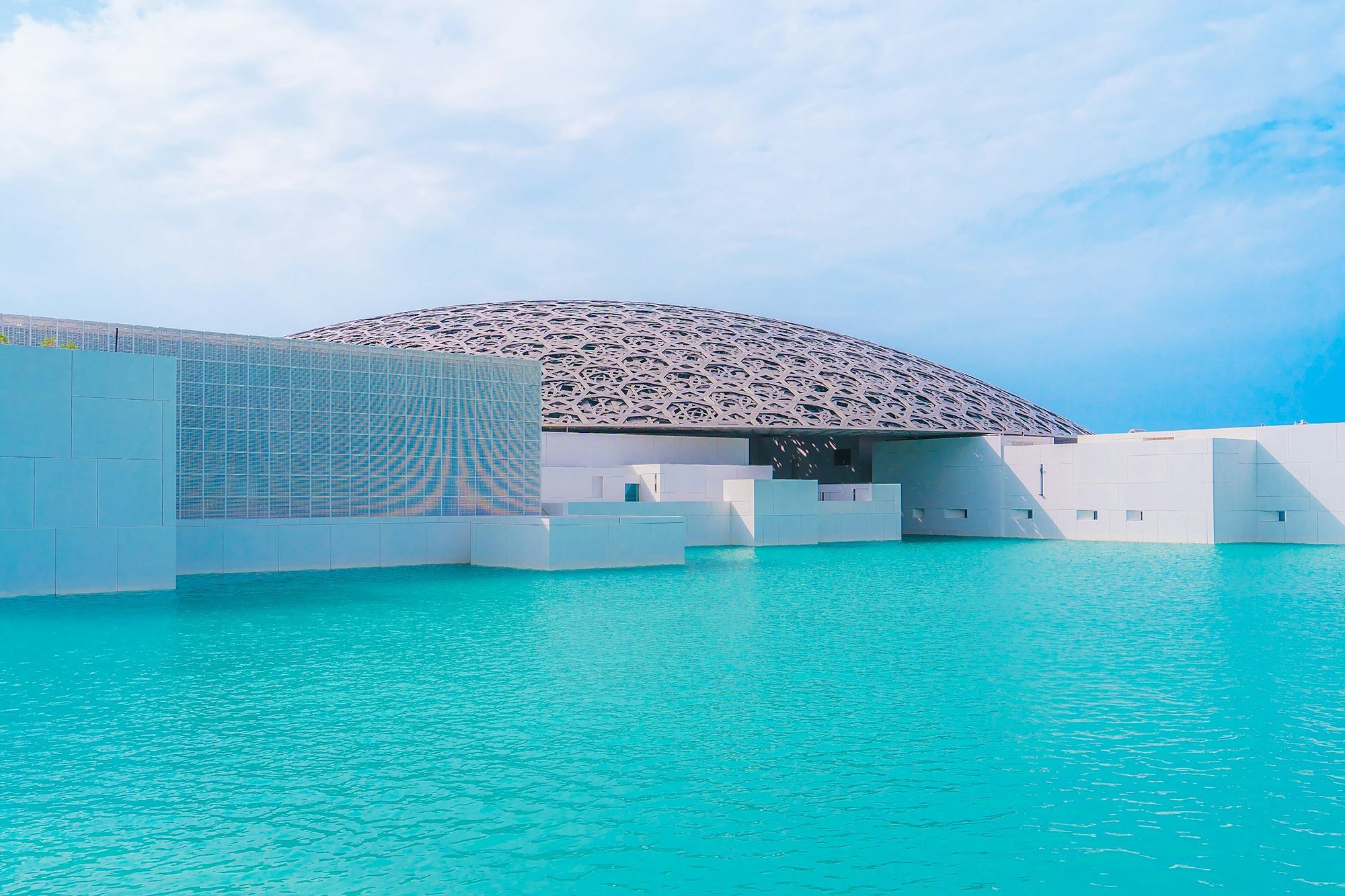 La cúpula de celosía del Louvre Abu Dhabi sobre aguas turquesas en la isla de Saadiyat