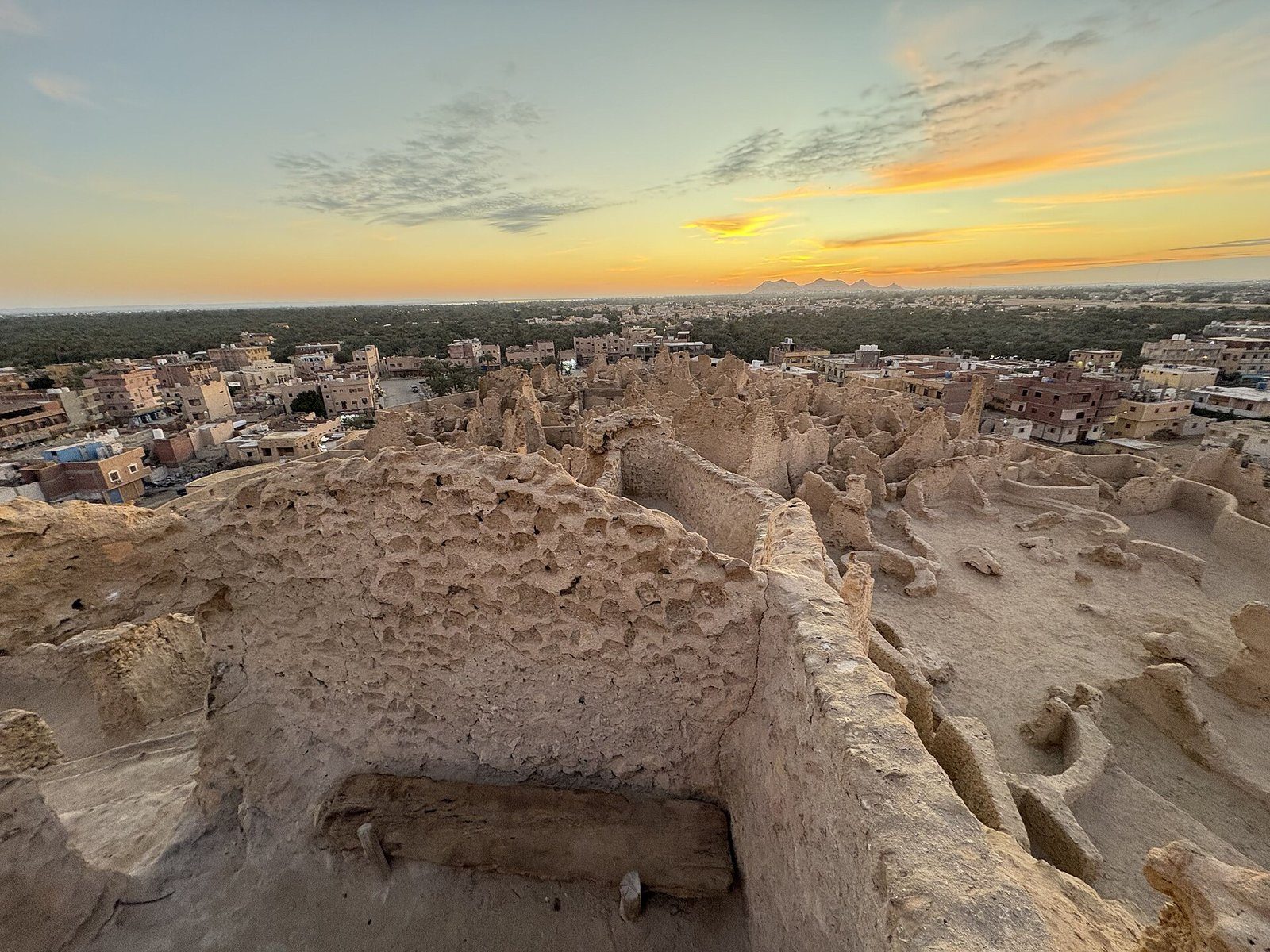 Las erosionadas ruinas de adobe de la fortaleza de Shali en el oasis de Siwa bajo un cielo dorado al atardecer.
