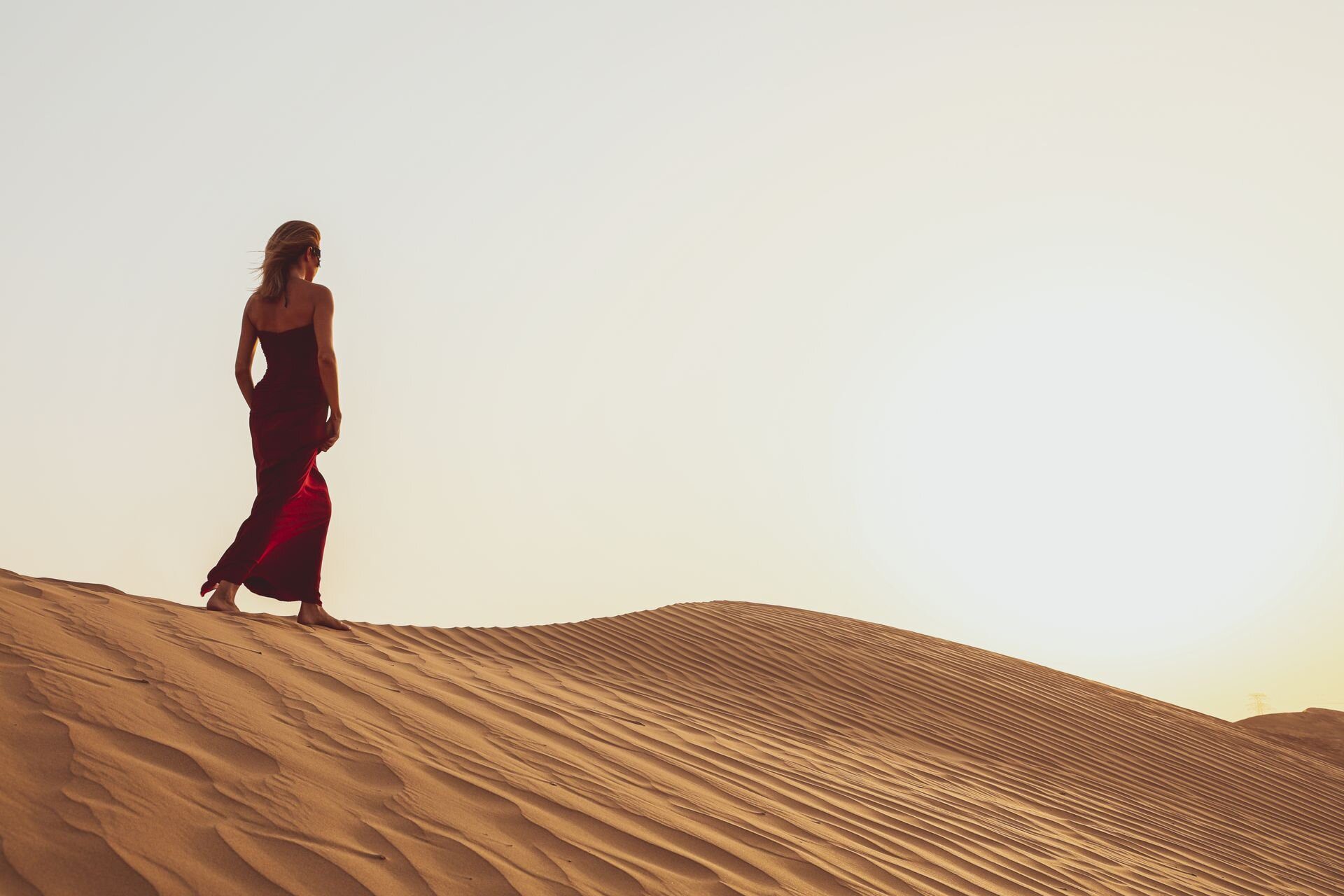 Una viajera con vestido rojo caminando por las dunas a las afueras de Dubái al atardecer