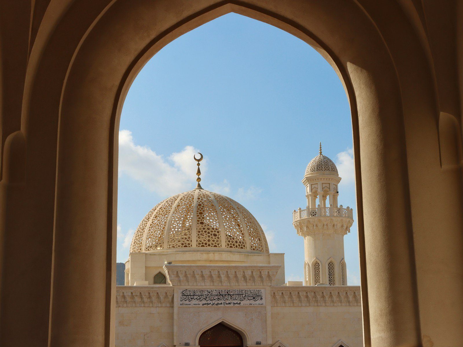 La cúpula dorada calada y un minarete de la Gran Mezquita del Sultán Qaboos enmarcados por un arco apuntado de arenisca, Mascate.