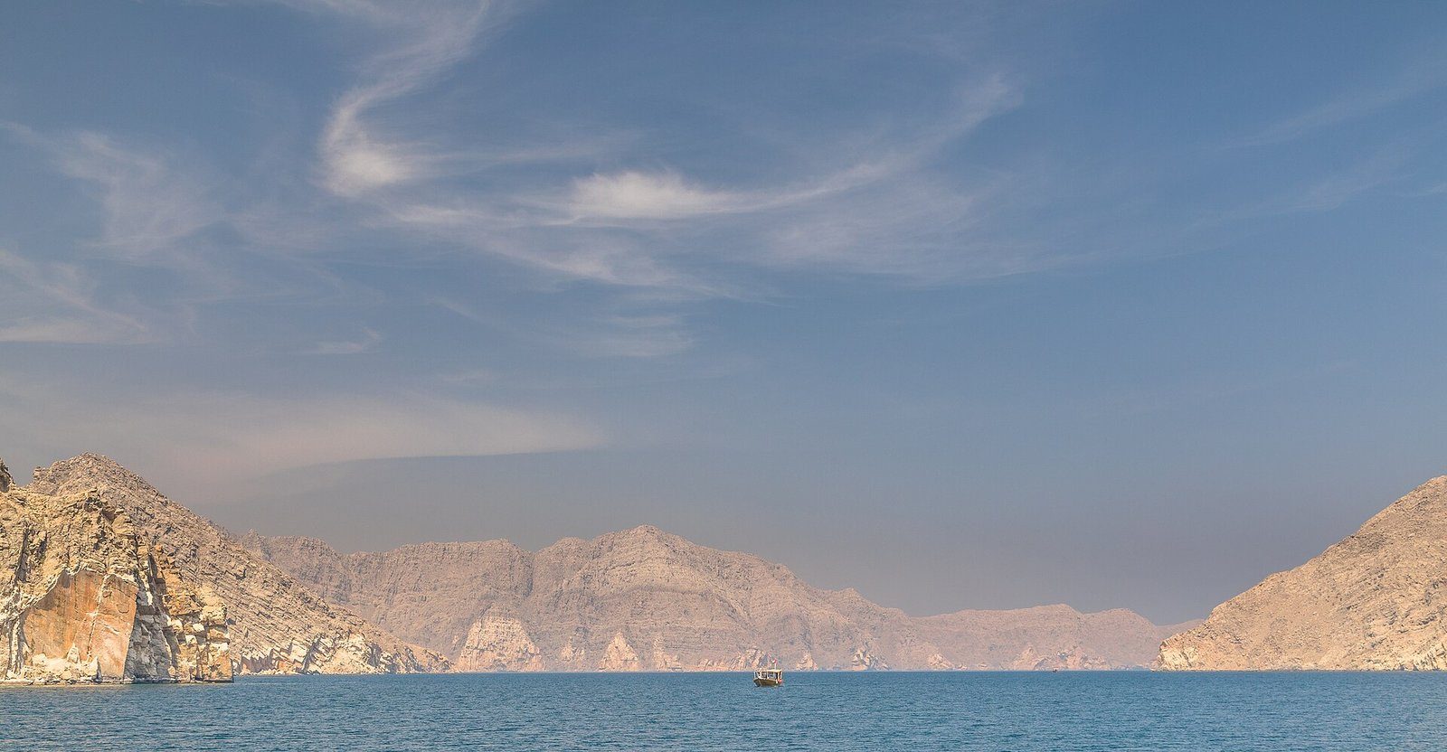 Un dhow solitario cruza las aguas tranquilas y turquesas de un fiordo entre las montañas de la península de Musandam, Omán.