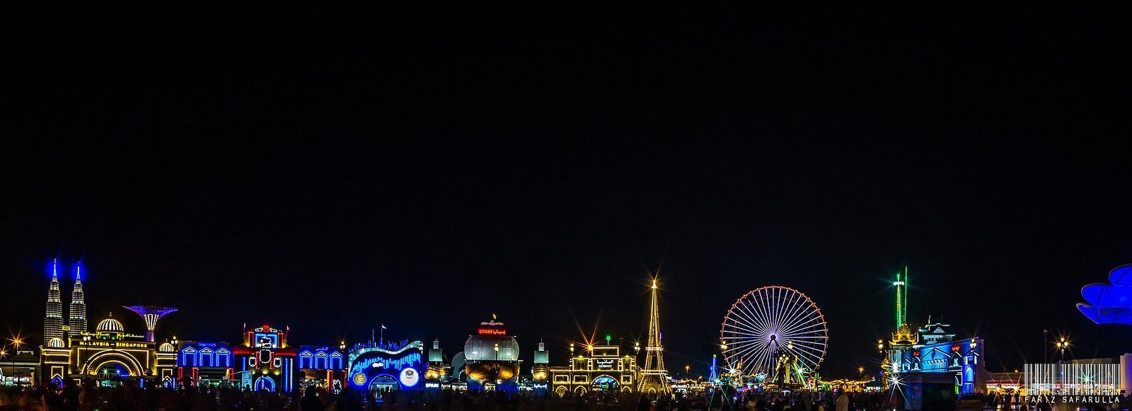 Los pabellones, torres y la noria iluminados de Global Village, Dubái, de noche.