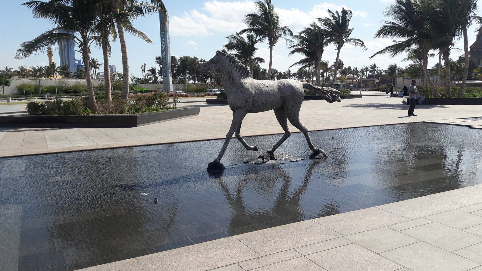 Una escultura de caballo sobre un estanque reflectante entre palmeras en la Corniche de Yeda, junto al Mar Rojo.
