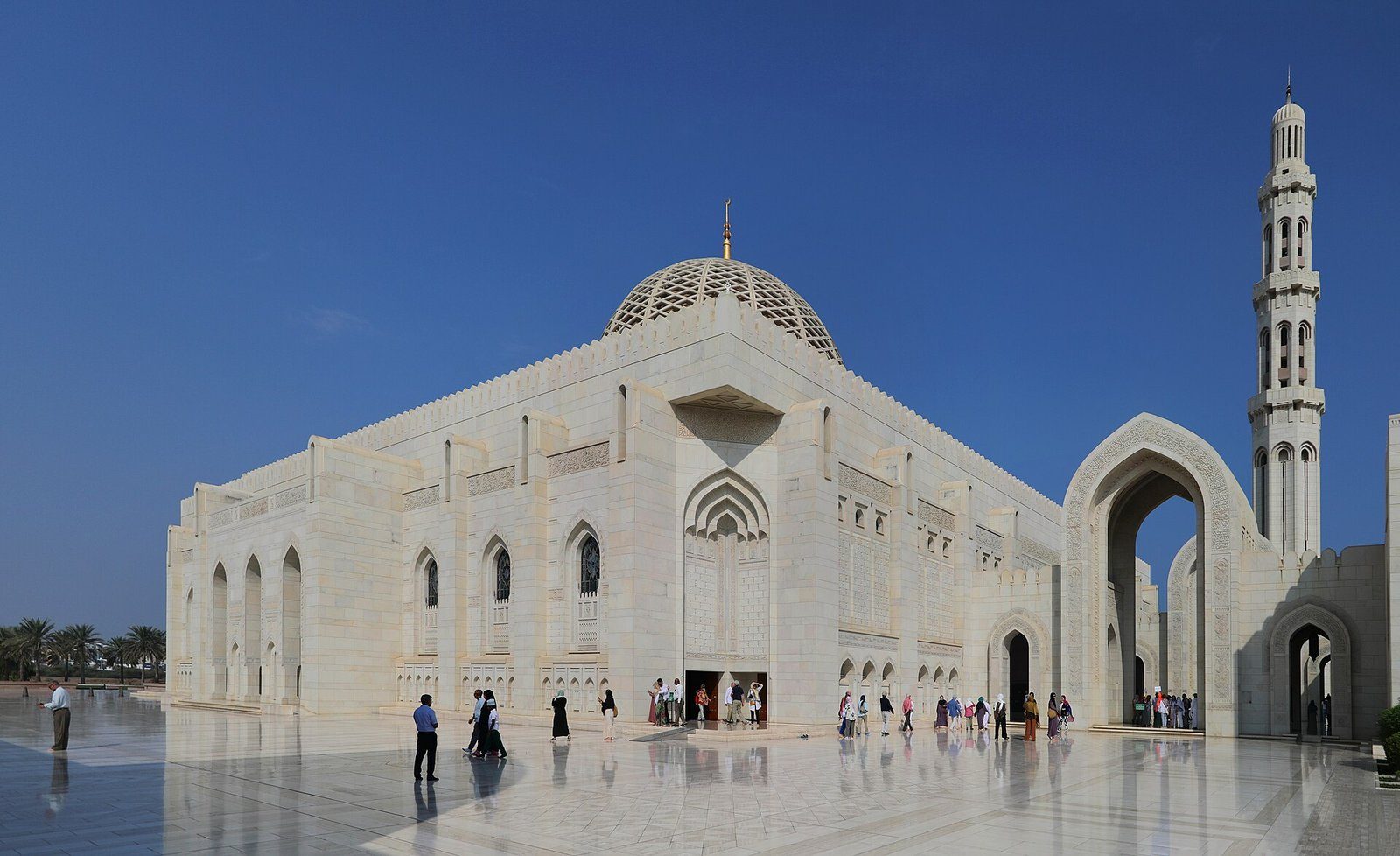 La sala de oración de mármol blanco y el minarete de la Gran Mezquita del Sultán Qaboos en Mascate bajo un cielo azul intenso.