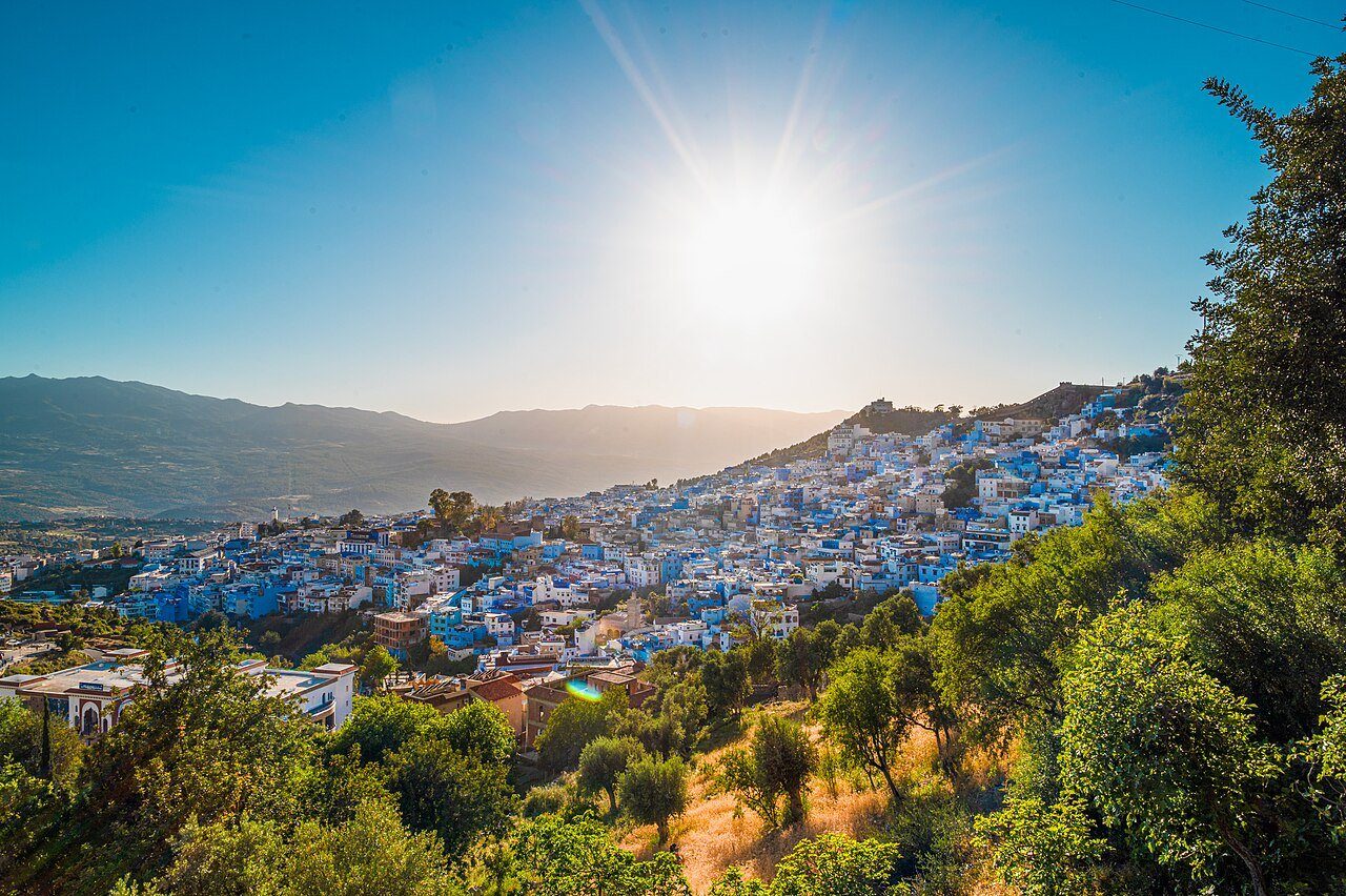 La ciudad de Chefchaouen, pintada de azul, extendida sobre las verdes laderas de las montañas del Rif bajo un sol radiante.