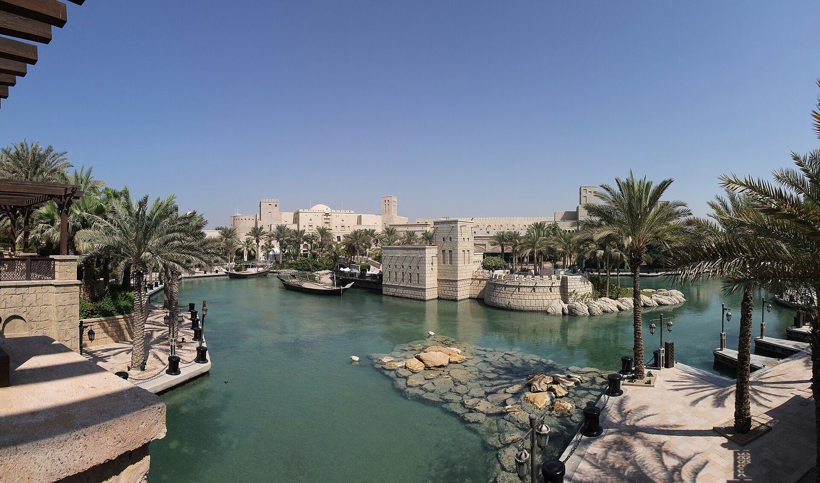 Los canales bordeados de palmeras y la arquitectura de torres de viento de Madinat Jumeirah en Dubái bajo un cielo azul despejado.