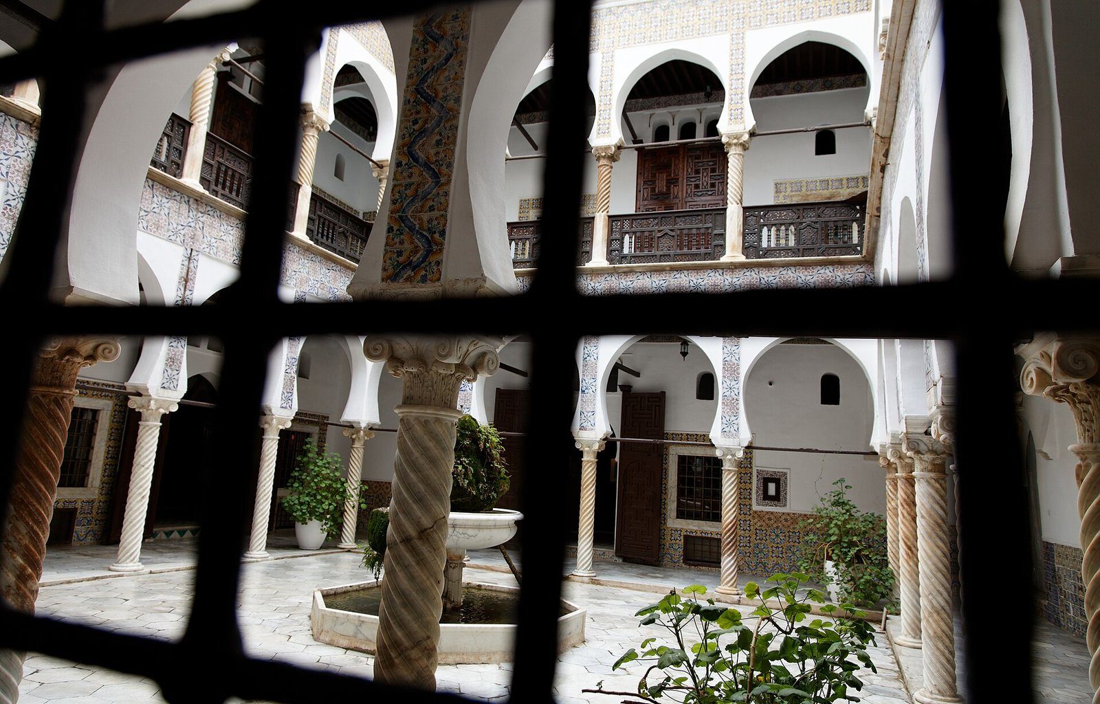 Las columnas talladas y los arcos de herradura de una casa con patio de la época otomana en la Casbah de Argel, entrevistos a través de la reja de hierro forjado de una ventana.