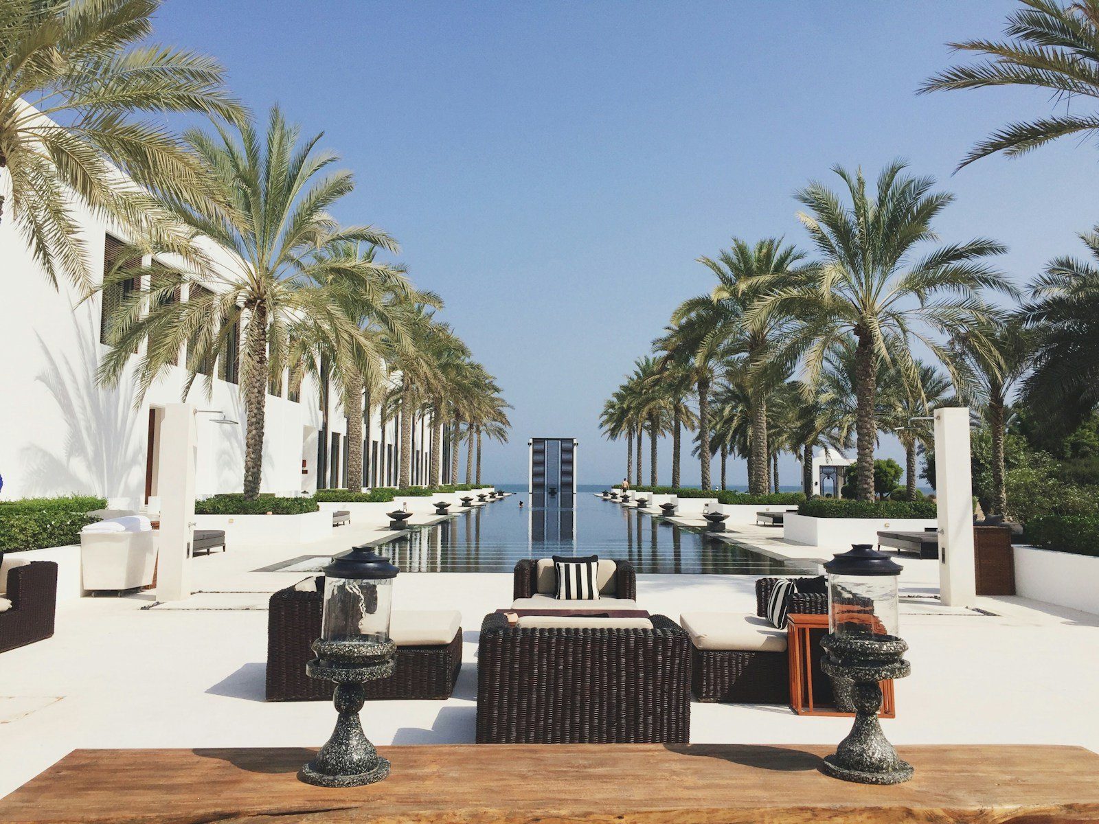Un largo estanque reflectante enmarcado por palmeras datileras y columnatas blancas se extiende hacia el mar en The Chedi Muscat, Omán.