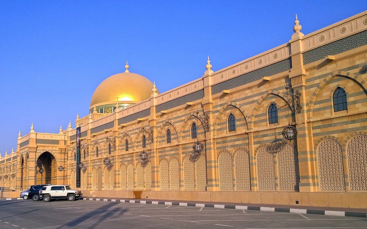 La cúpula dorada y las arcadas de piedra rayada del Museo de la Civilización Islámica de Sharjah brillan bajo un cielo azul intenso.