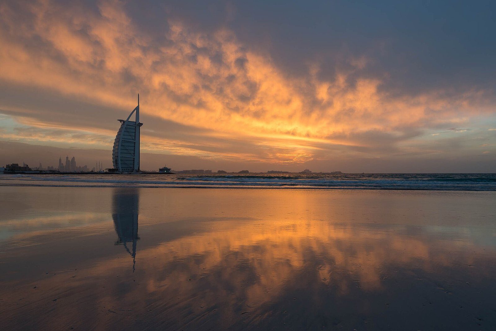 La silueta del Burj Al Arab ante un cielo de atardecer encendido, reflejada en la arena húmeda de Jumeirah Beach.