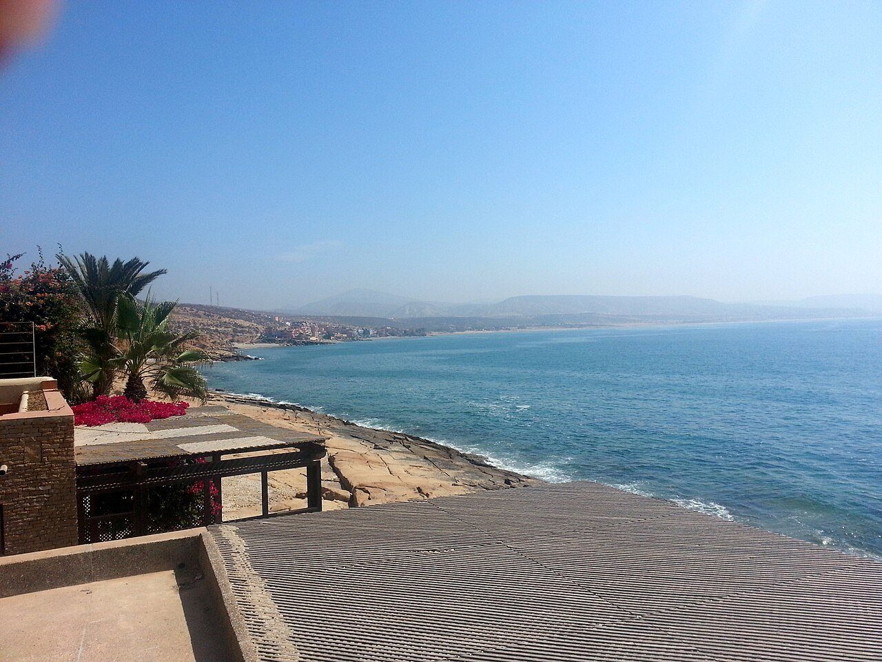 Una terraza a la sombra de las palmeras sobre la costa atlántica de Taghazout, Marruecos, en un día claro y luminoso.