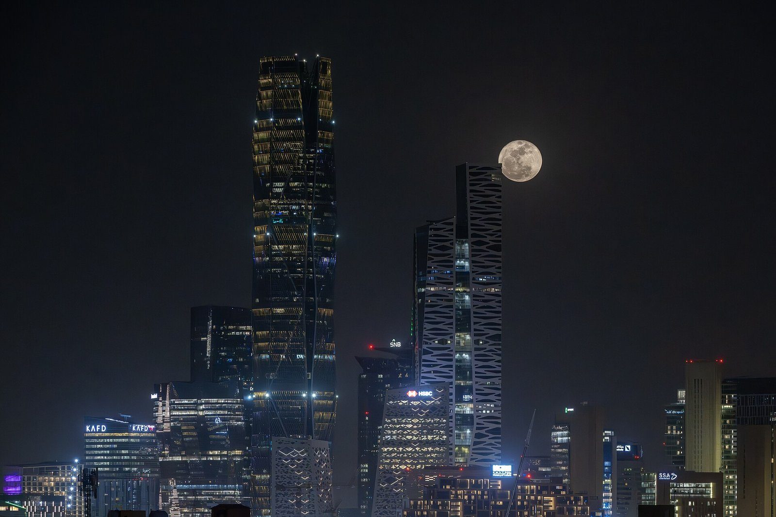 Las torres de vidrio del King Abdullah Financial District en Riad iluminadas de noche bajo la luna llena.