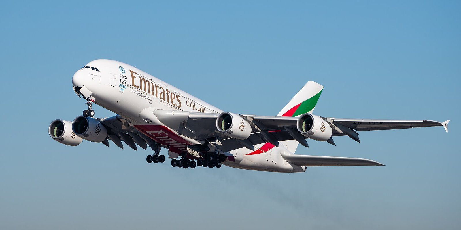 Un Airbus A380 de Emirates en ascenso tras el despegue contra un cielo azul pálido.