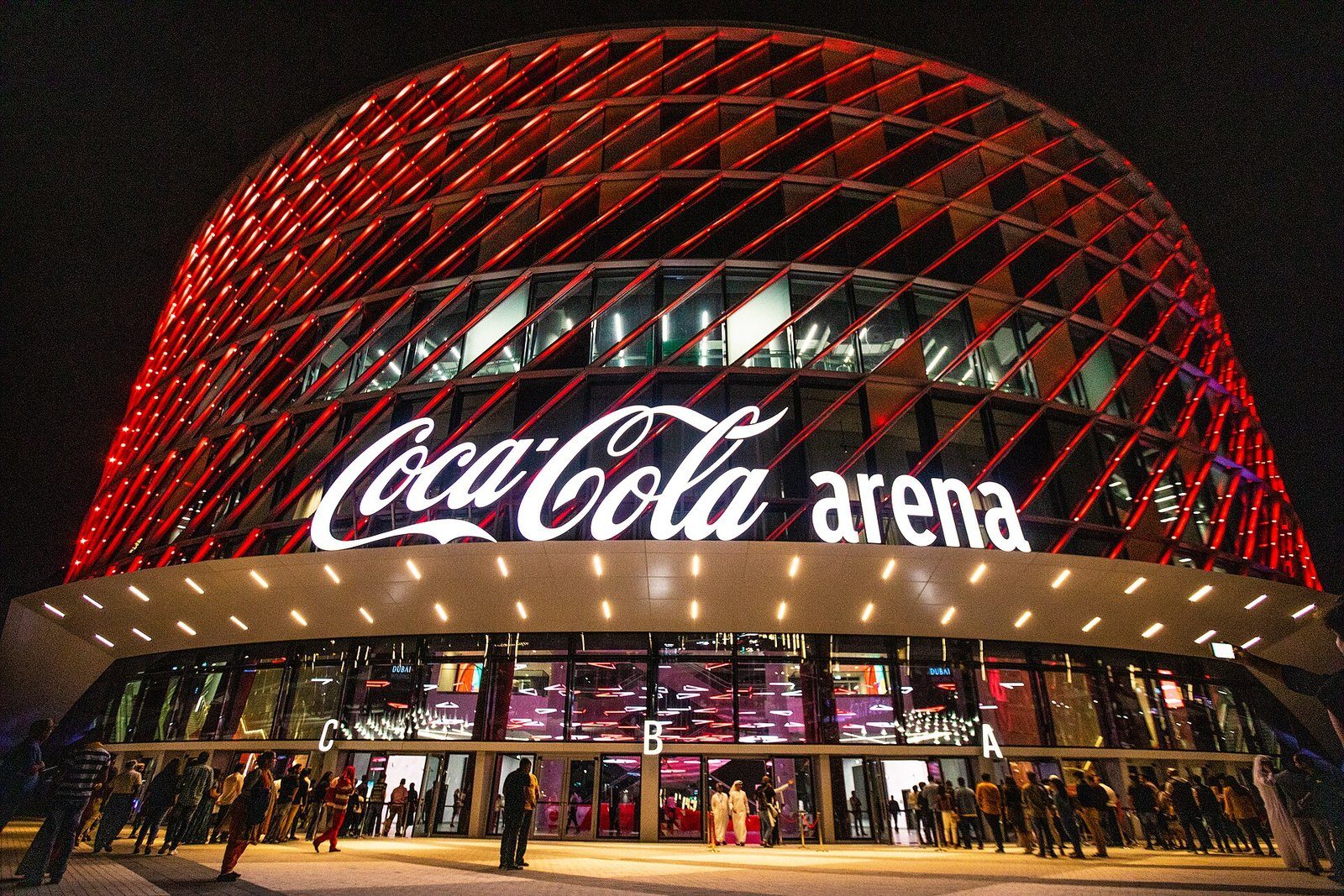 La fachada de celosía iluminada en rojo del Coca-Cola Arena resplandece sobre su entrada de noche en Dubái.
